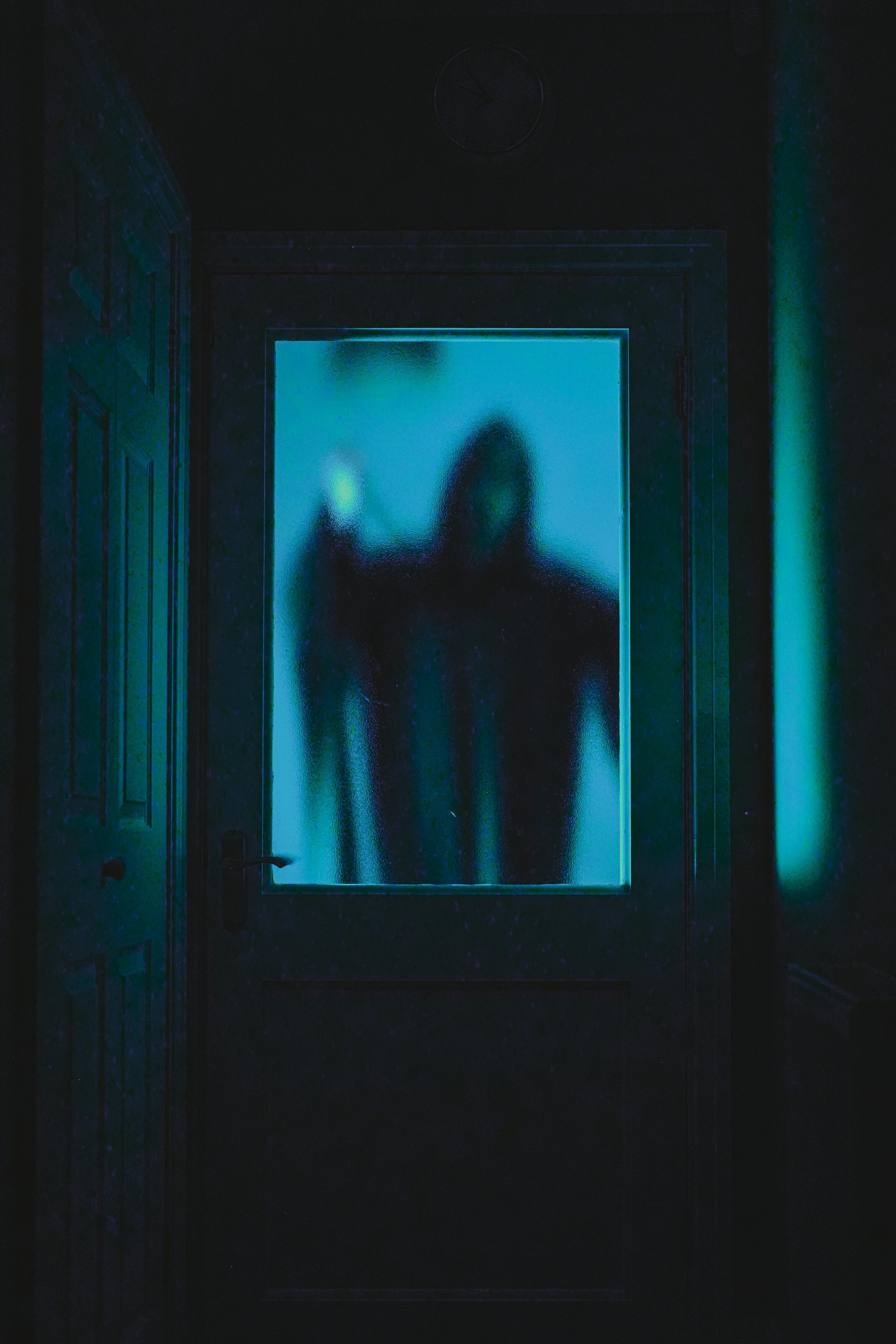 Reaper in Scream mask down a dark hallway behind a blue glass door