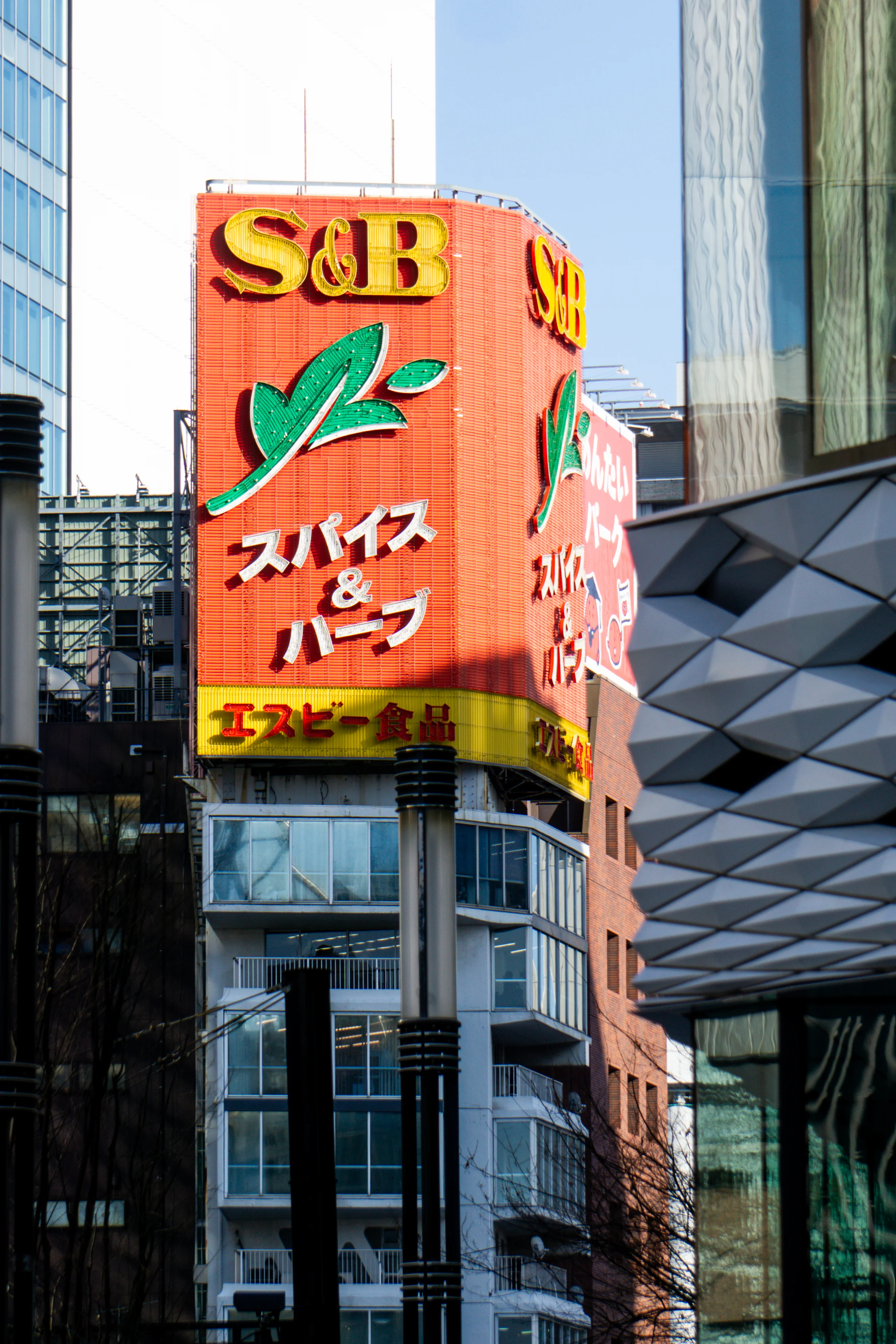 Bright orange sign with text in Japanese above a small glass building.
