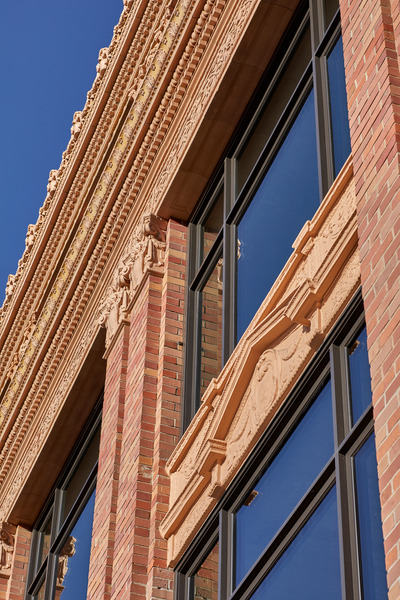Close-up of a historic brick building facade with detailed terracotta ornamentation and large modern windows against a clear blue sky.