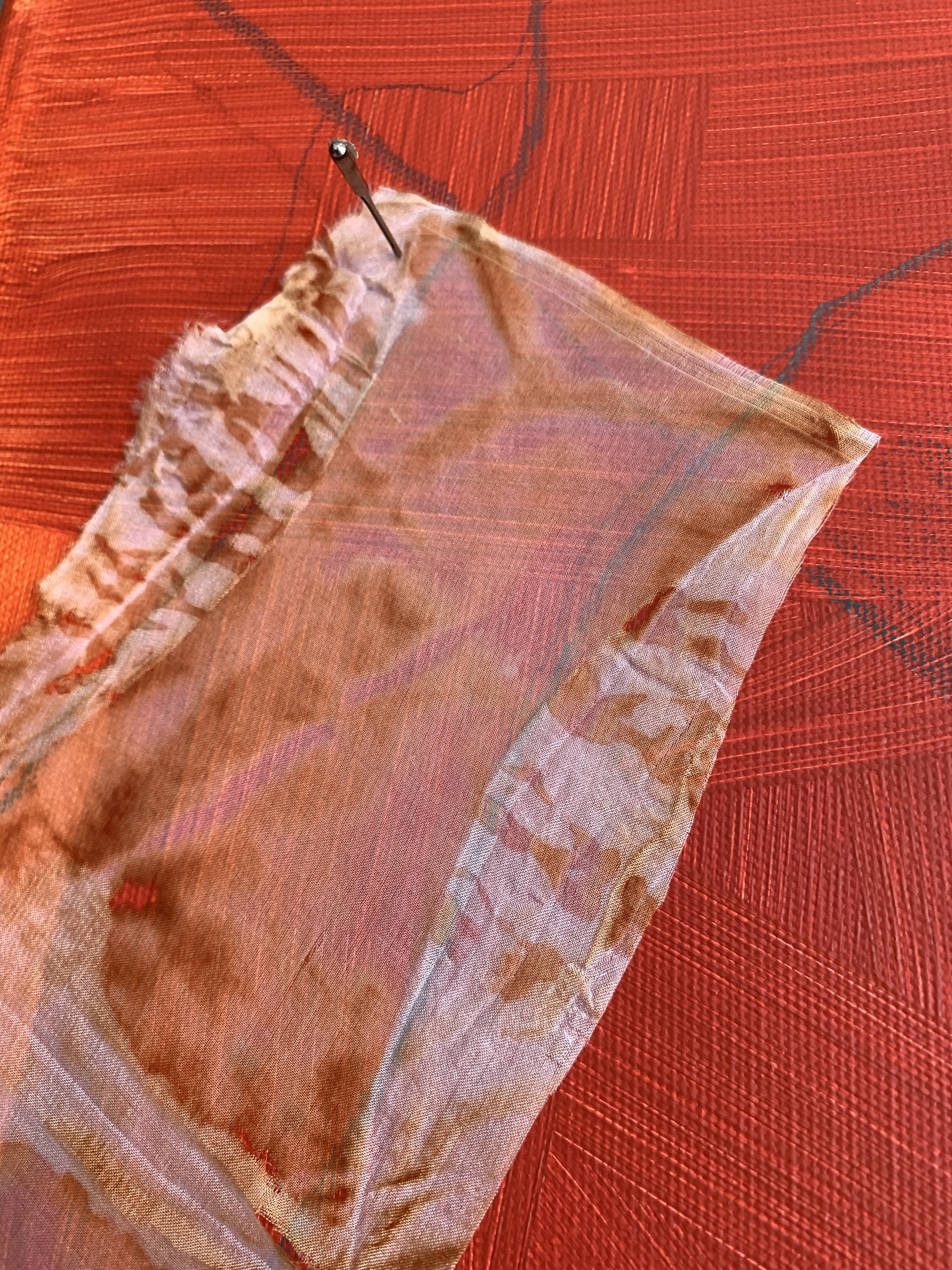 A scrap of pink dyed fabric pinned to a red background