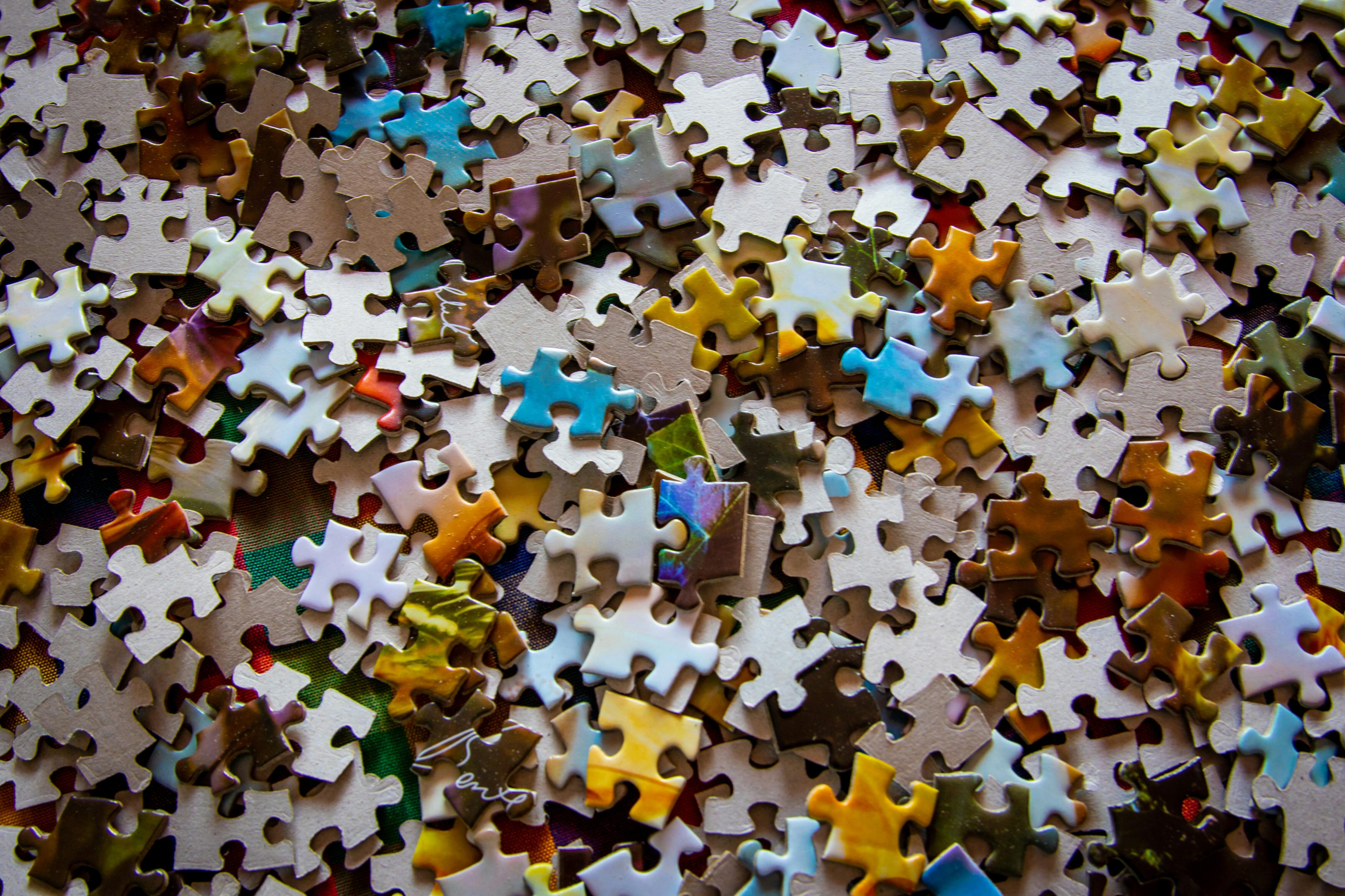 A close-up view of scattered jigsaw puzzle pieces in various colors, including yellow, blue, brown, and white, creating a textured and colorful pattern across the surface.