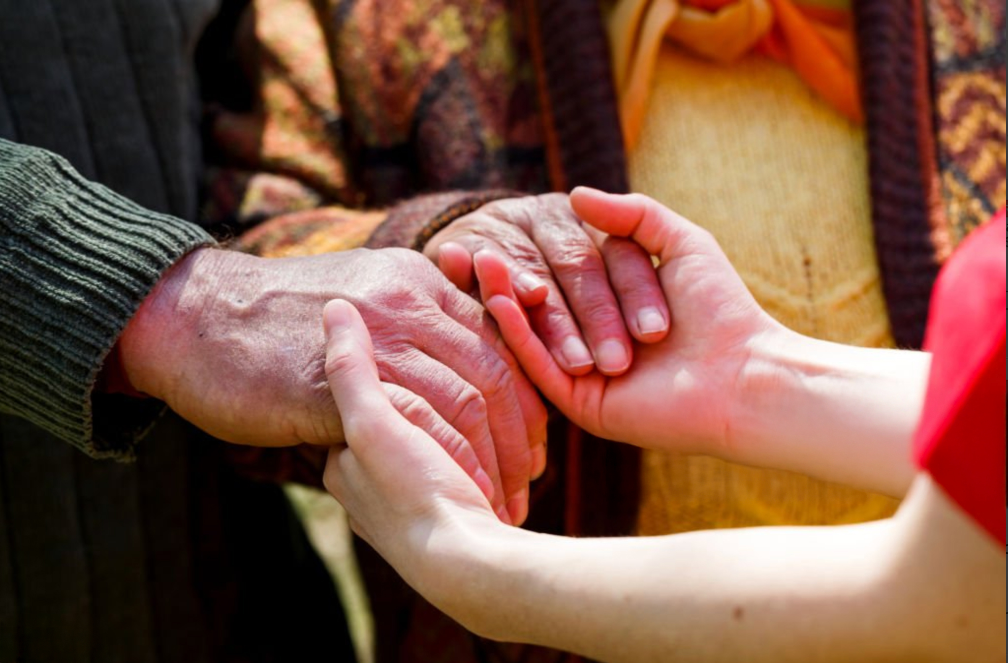 Close-up of three people’s hands gently clasped together in a gesture of care and support.