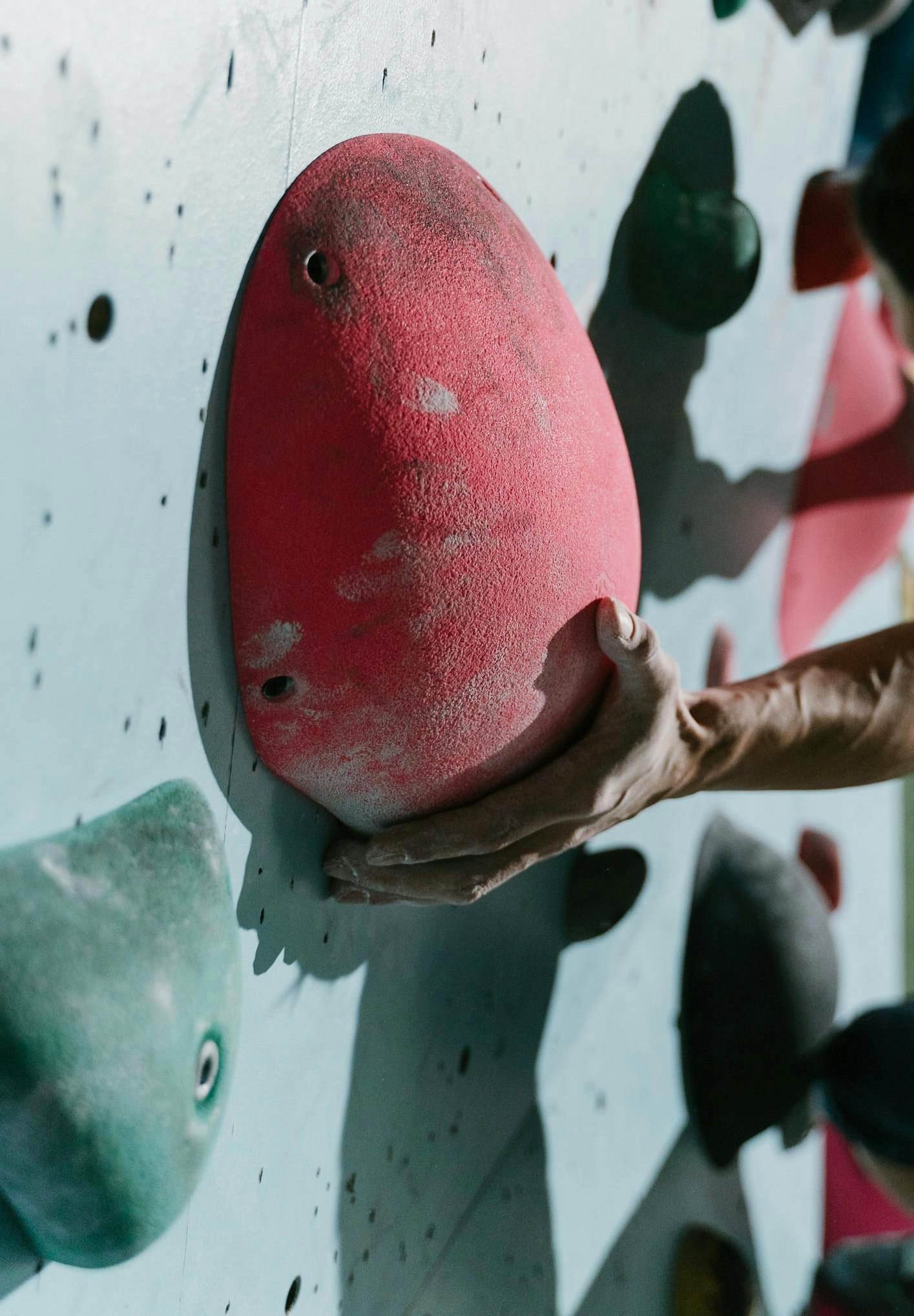 A hand gripping the underside of a pink climbing hold