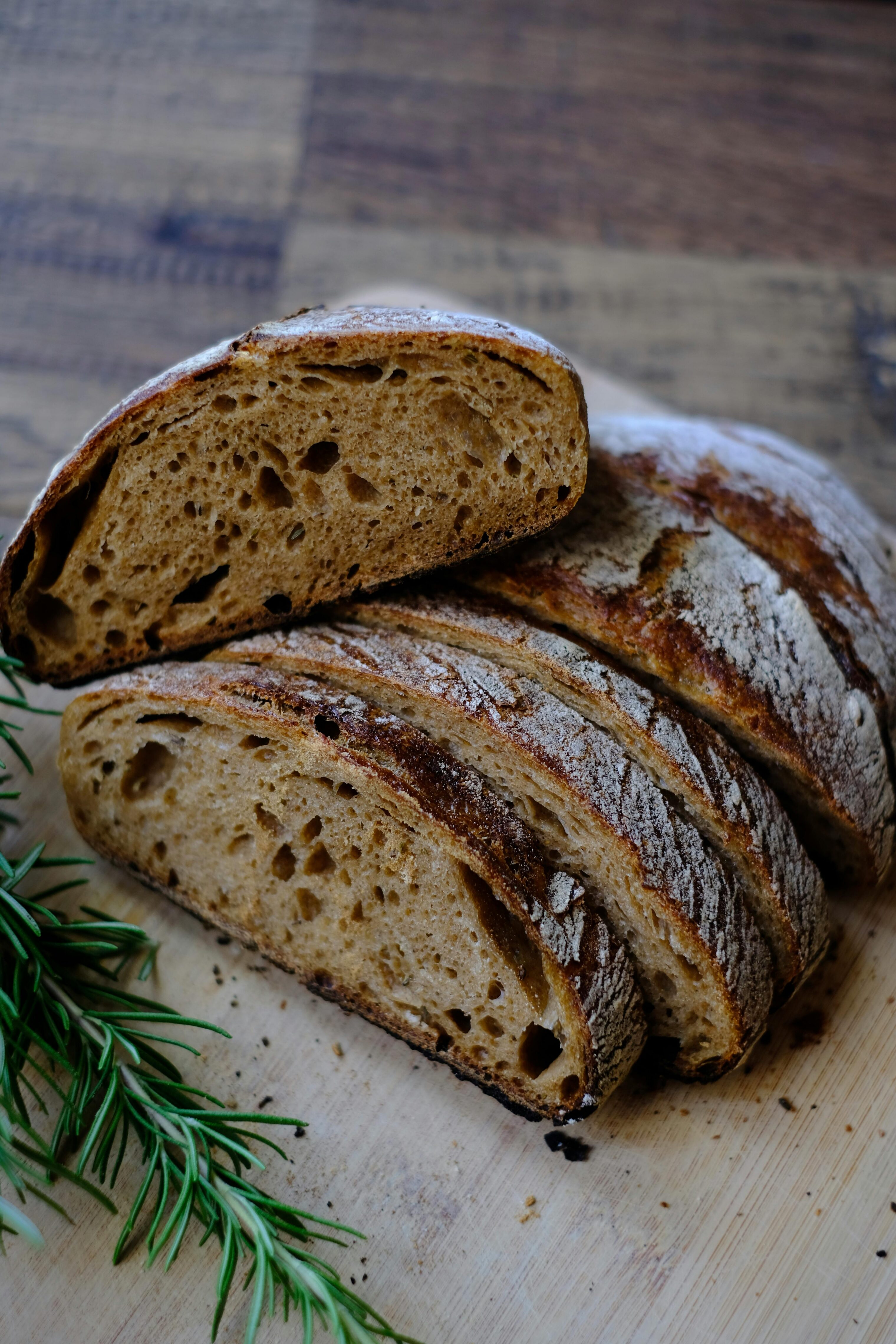 A sliced loaf of brown sourdough, a sprig of rosemary lies next to it.