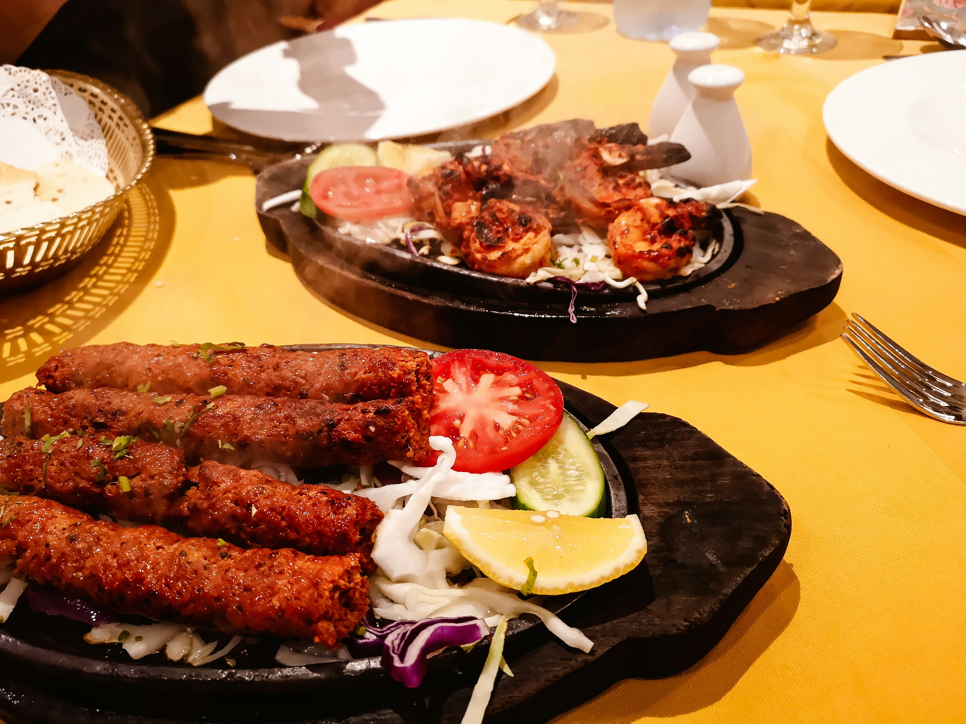 Plates with vegetables and meat skewers on a yellow table