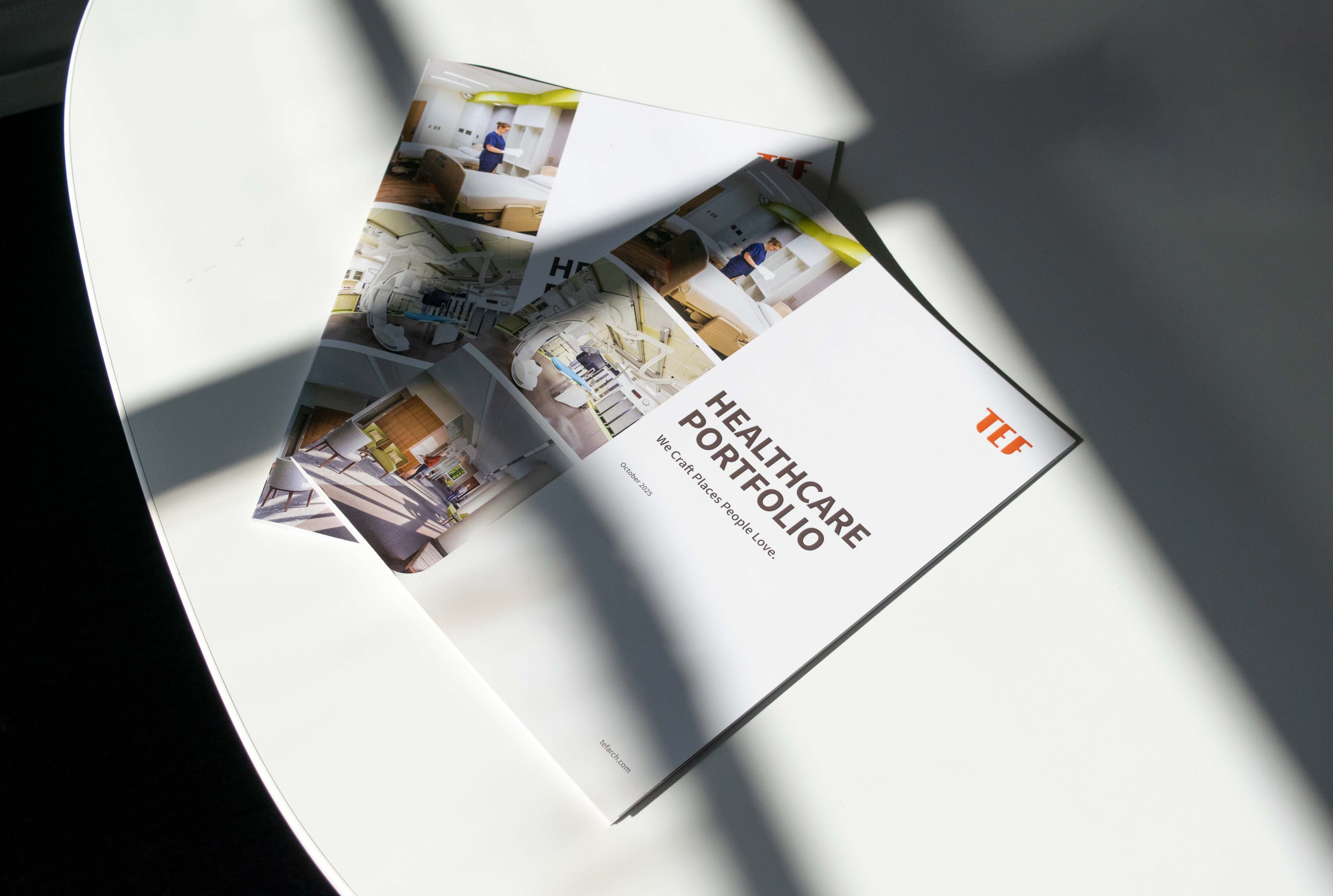 Two glossy booklets sitting on a white table in the crossed shadow of a window
