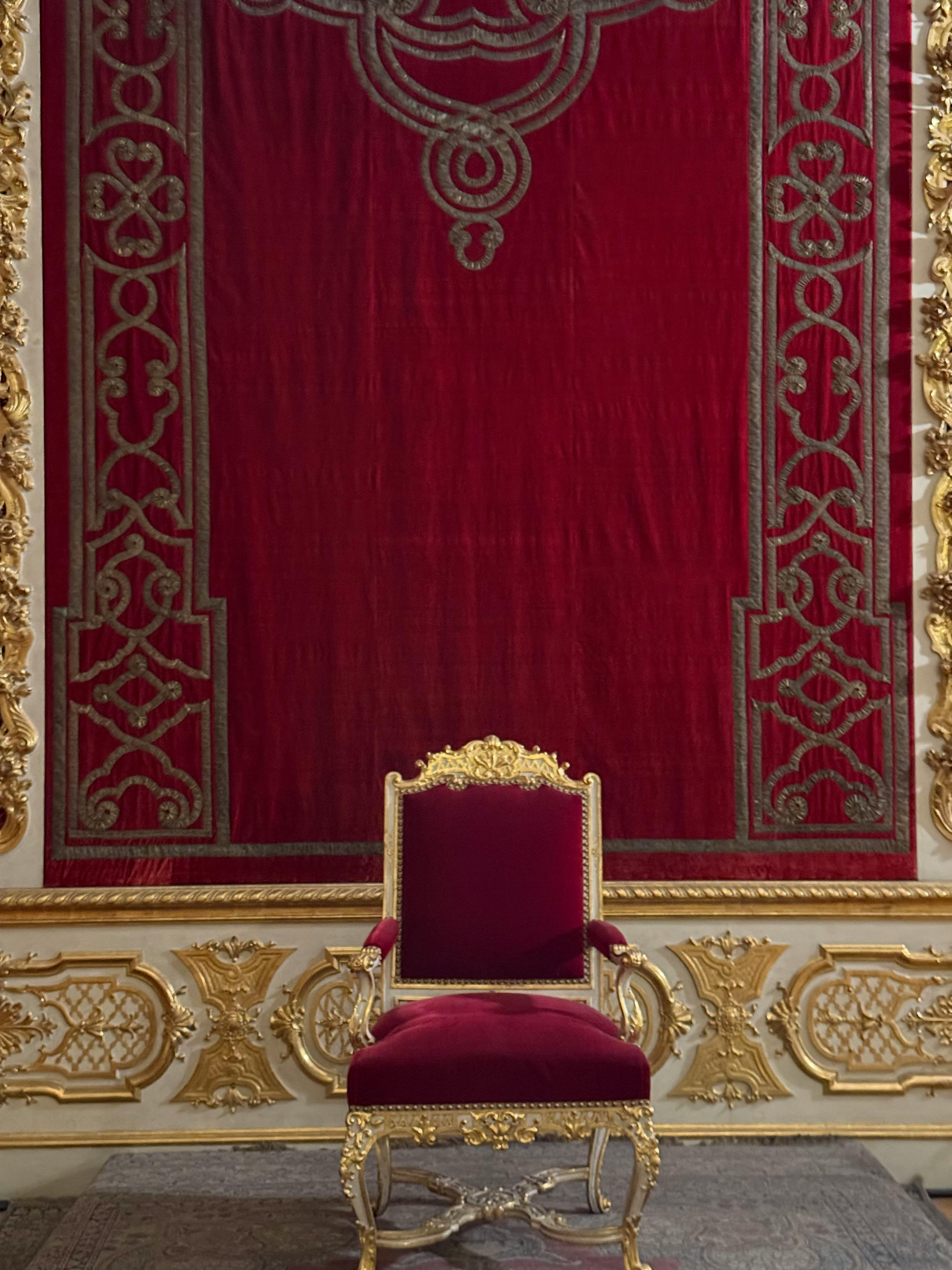 A red royal throne in front of a red tapestry