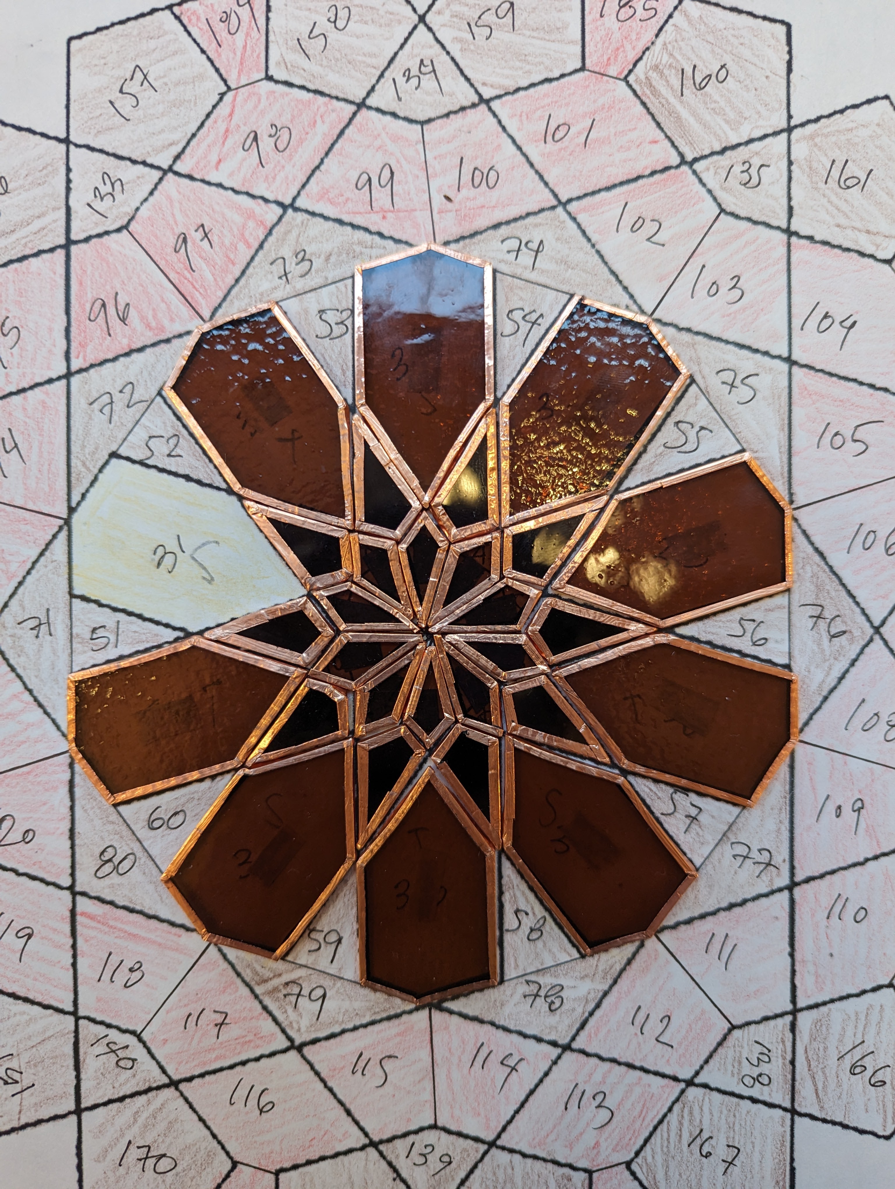 Small glass pieces laid out in a symmetrical circular pattern on a paper that dictates the pattern