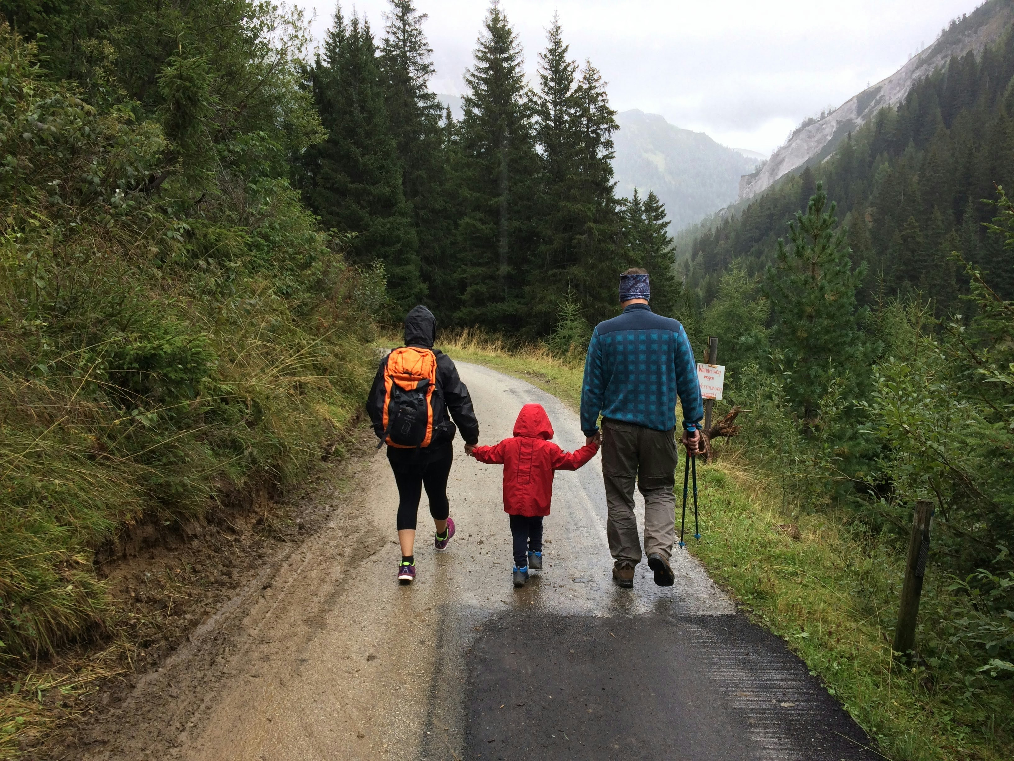 A mother, father, and child fro behind, walking on a forested road