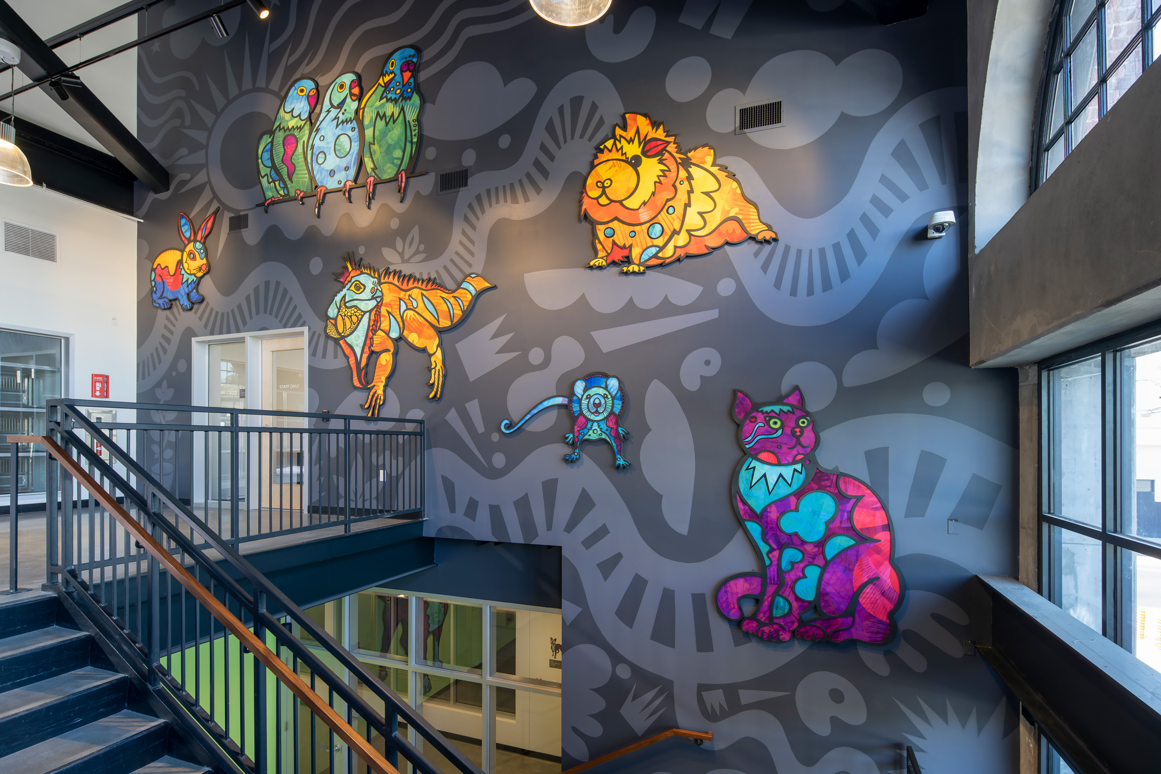 Large-scale, colorful animal-themed wall art animates a multi-story interior stairwell, integrating playful imagery and pattern into a shared circulation space filled with natural light.