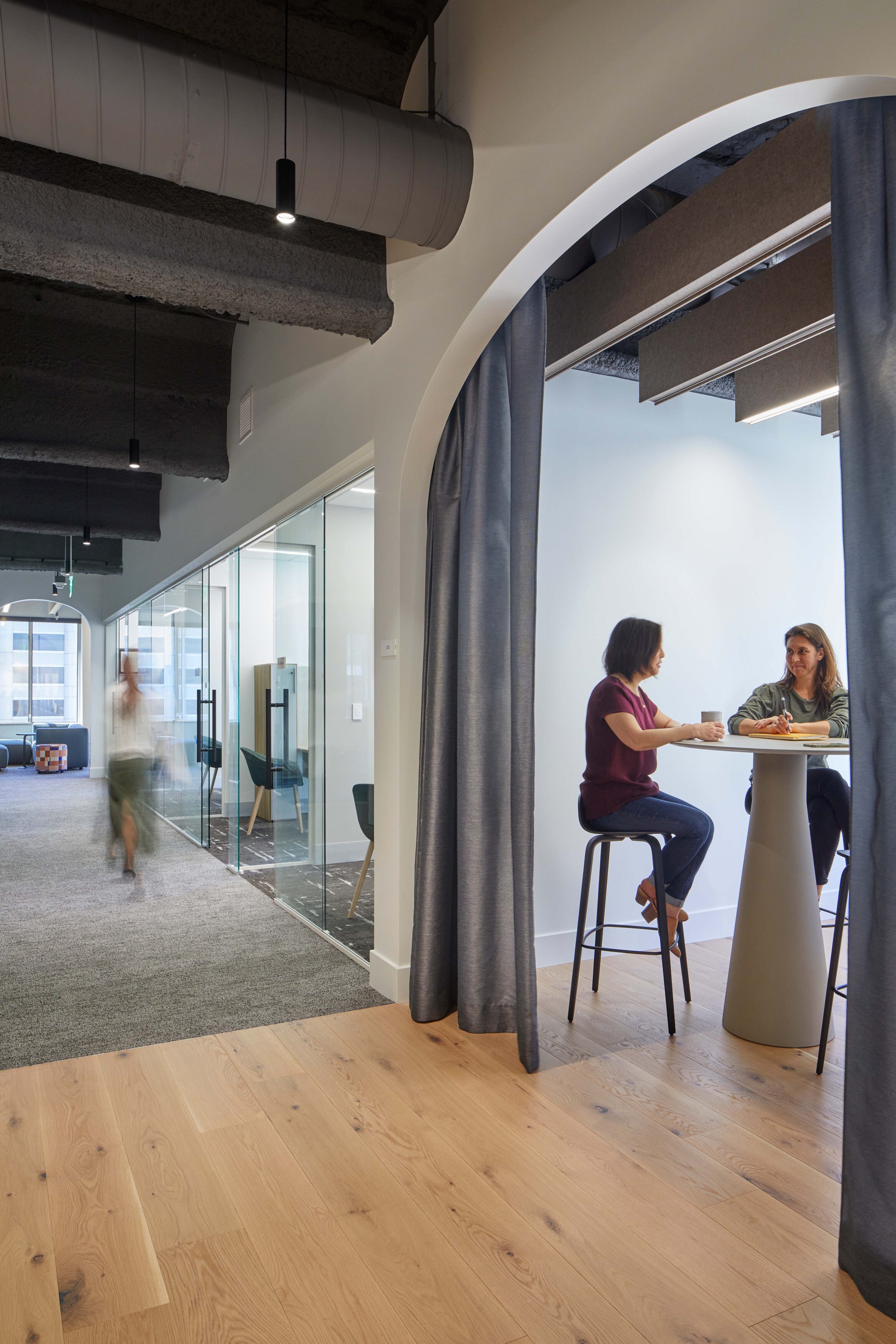 Small meeting alcove framed by an arched opening where two colleagues sit at a high table for a discussion.