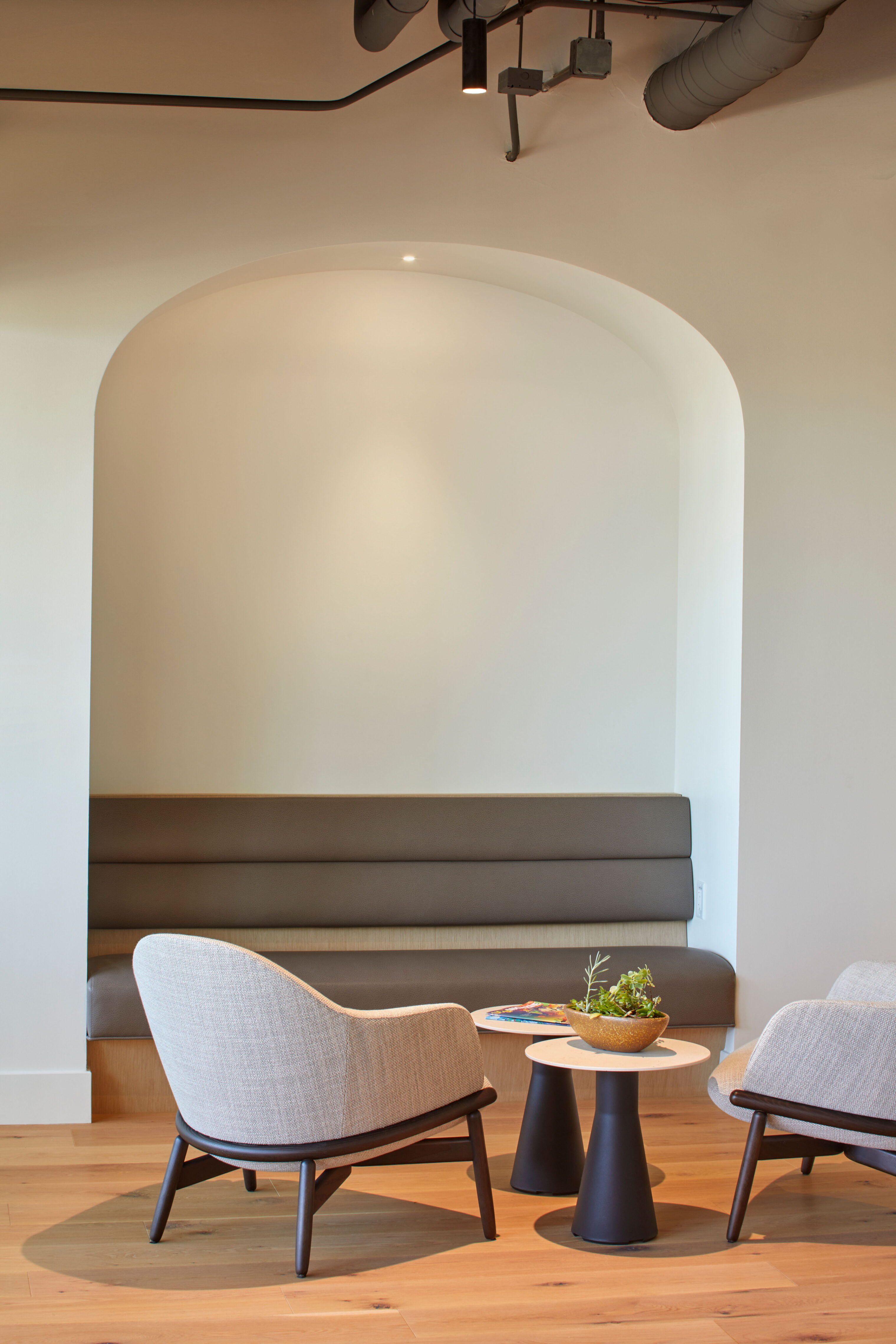Small lounge nook with upholstered bench seating set within an arched wall recess and two lounge chairs around a side table.