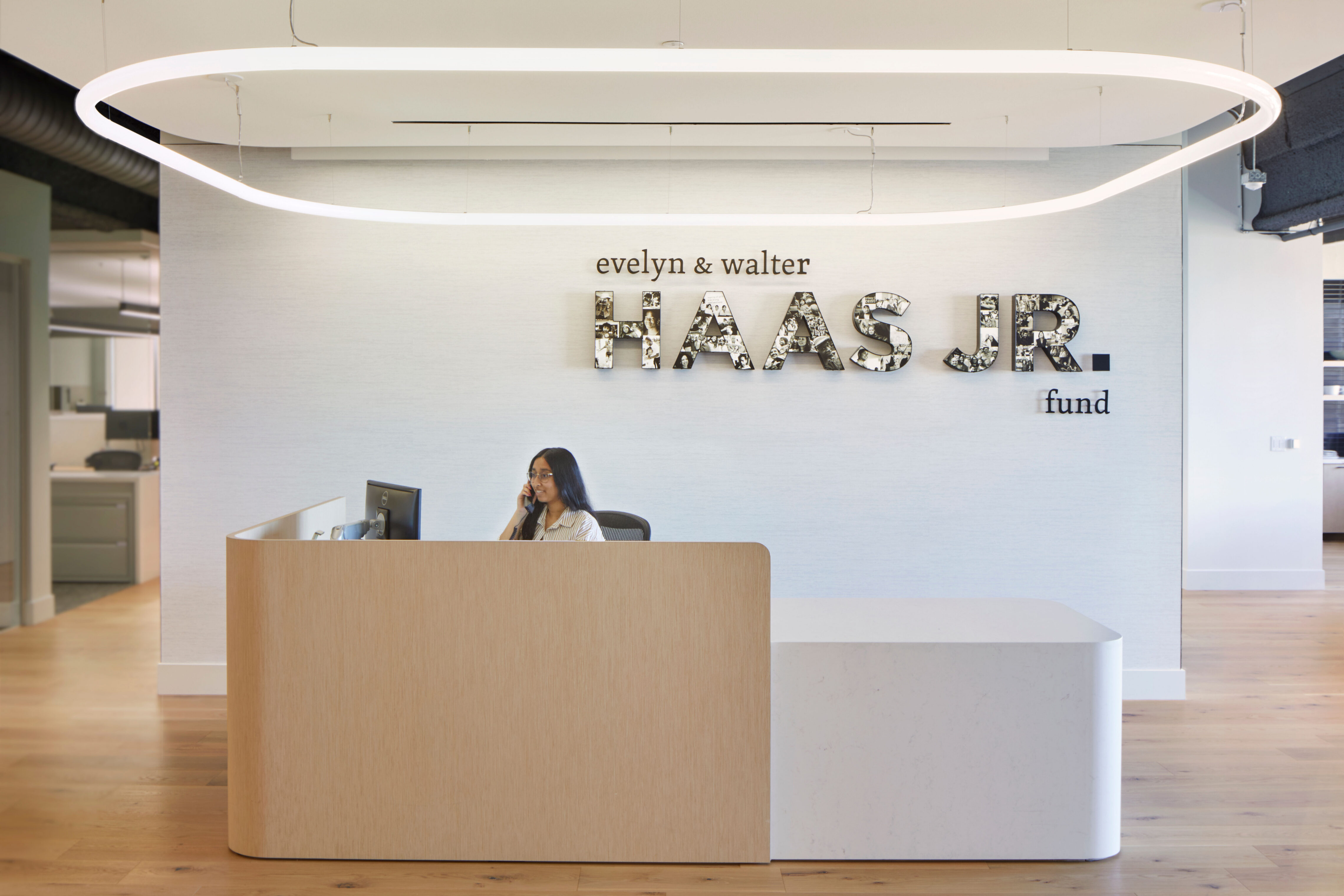 Reception area of the Evelyn & Walter Haas, Jr. Fund office featuring a curved wood desk beneath a large circular light fixture and a wall sign displaying the organization’s name.