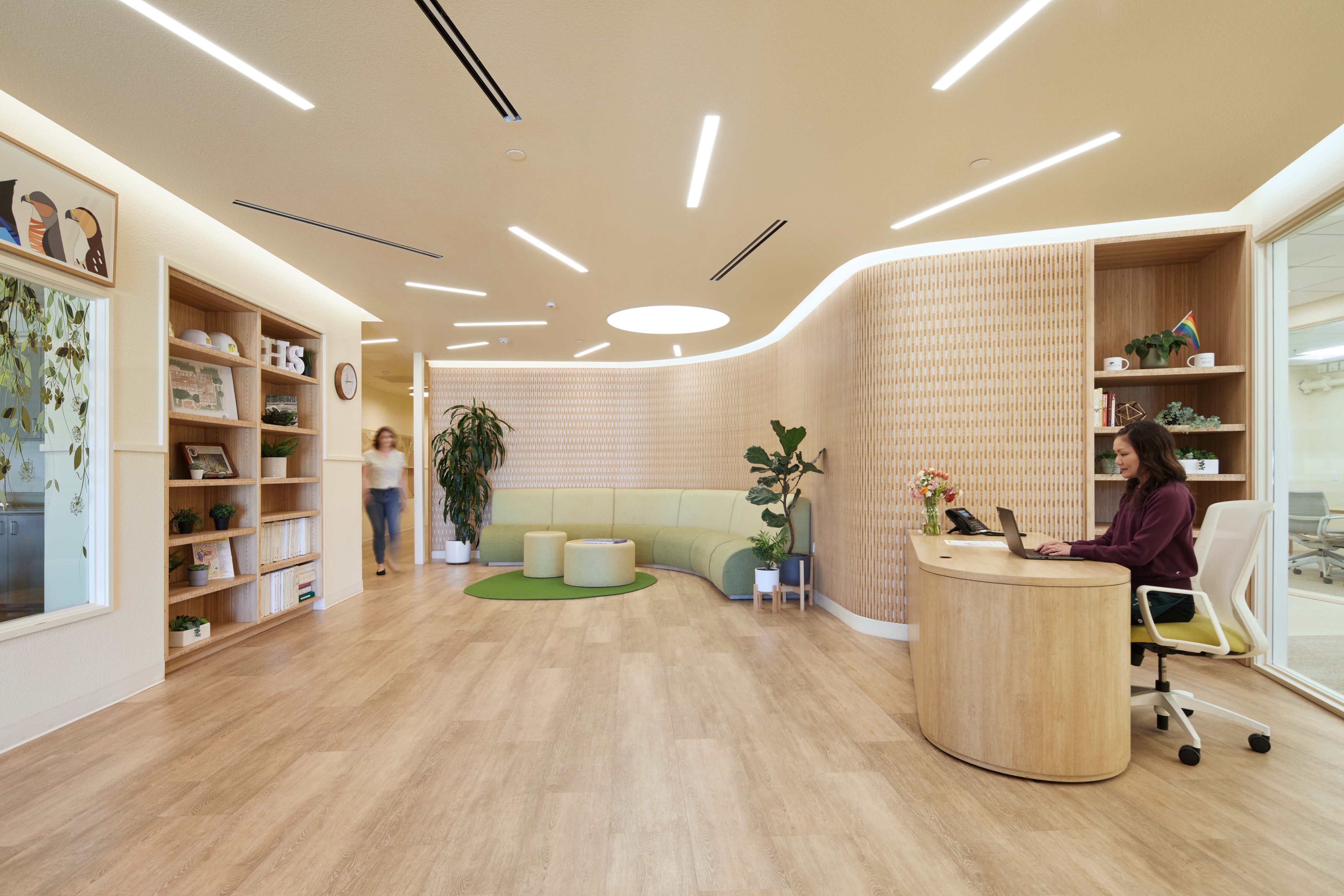 Reception desk and curved seating area in a warm, wood-accented school lobby with integrated shelving and soft lighting.