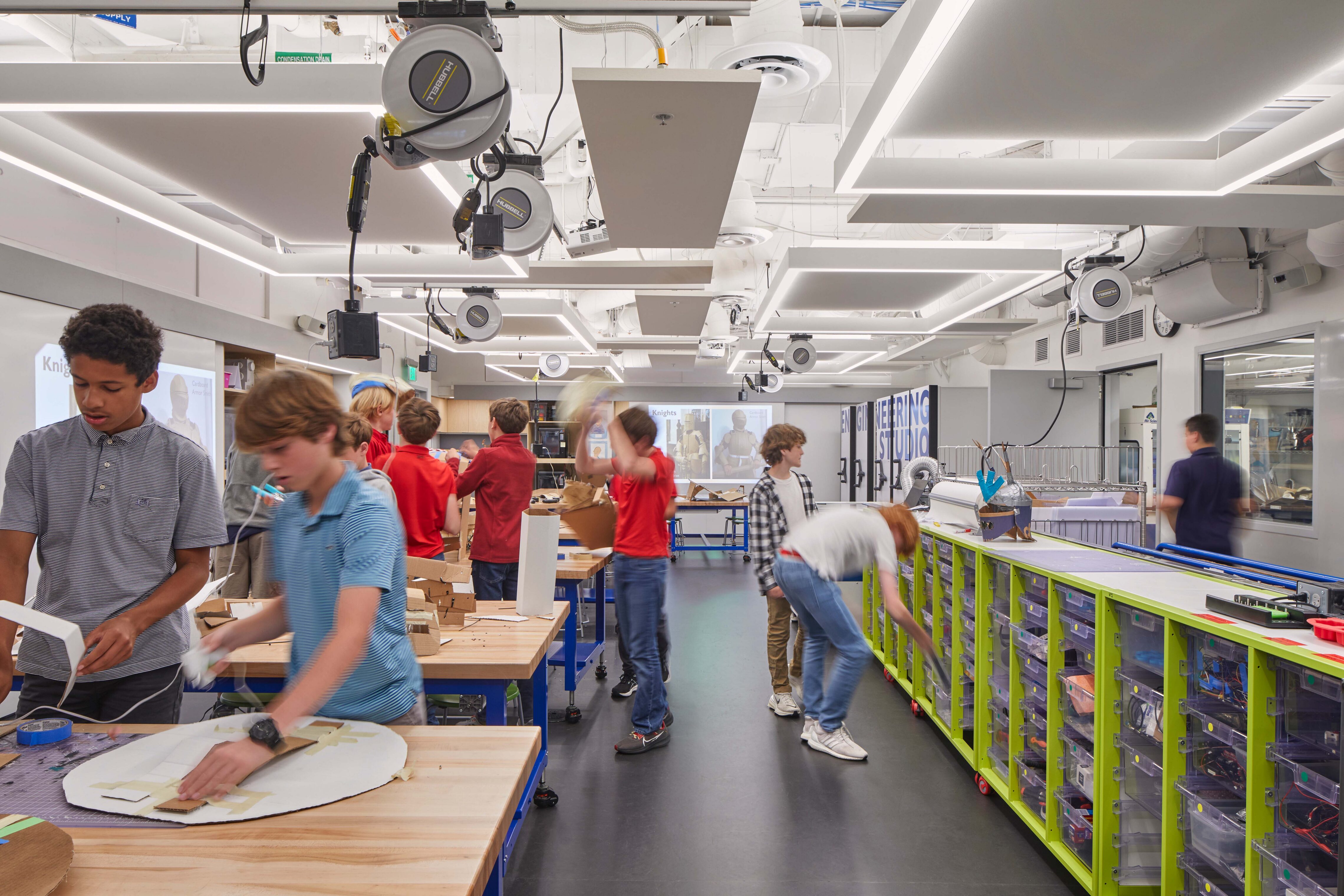 Students gather around worktables while accessing organized storage and tools along a wall of labeled parts bins in the Engineering Studio.