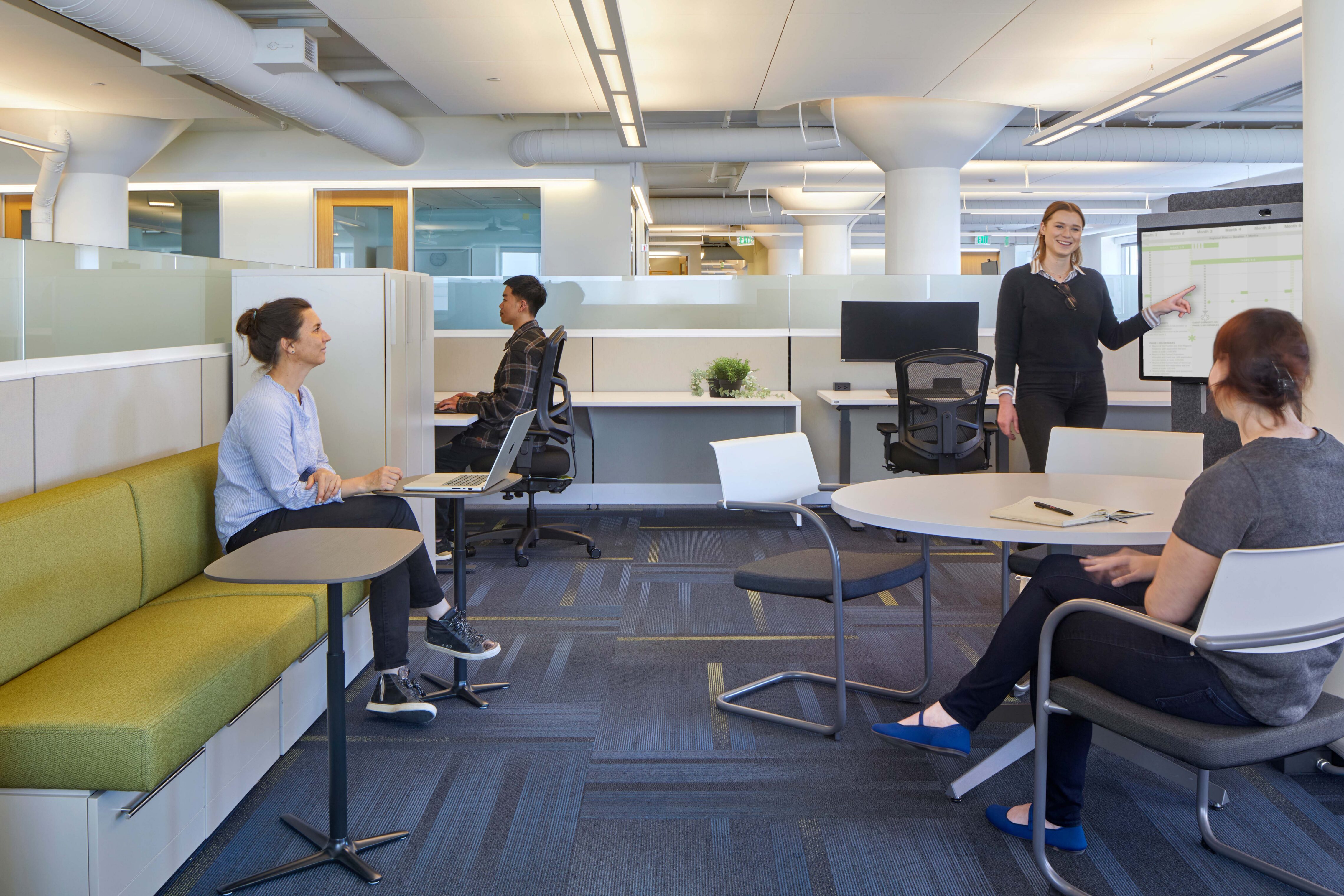 Open office lounge with flexible seating, workstations, and a presentation screen, supporting both individual work and informal collaboration.