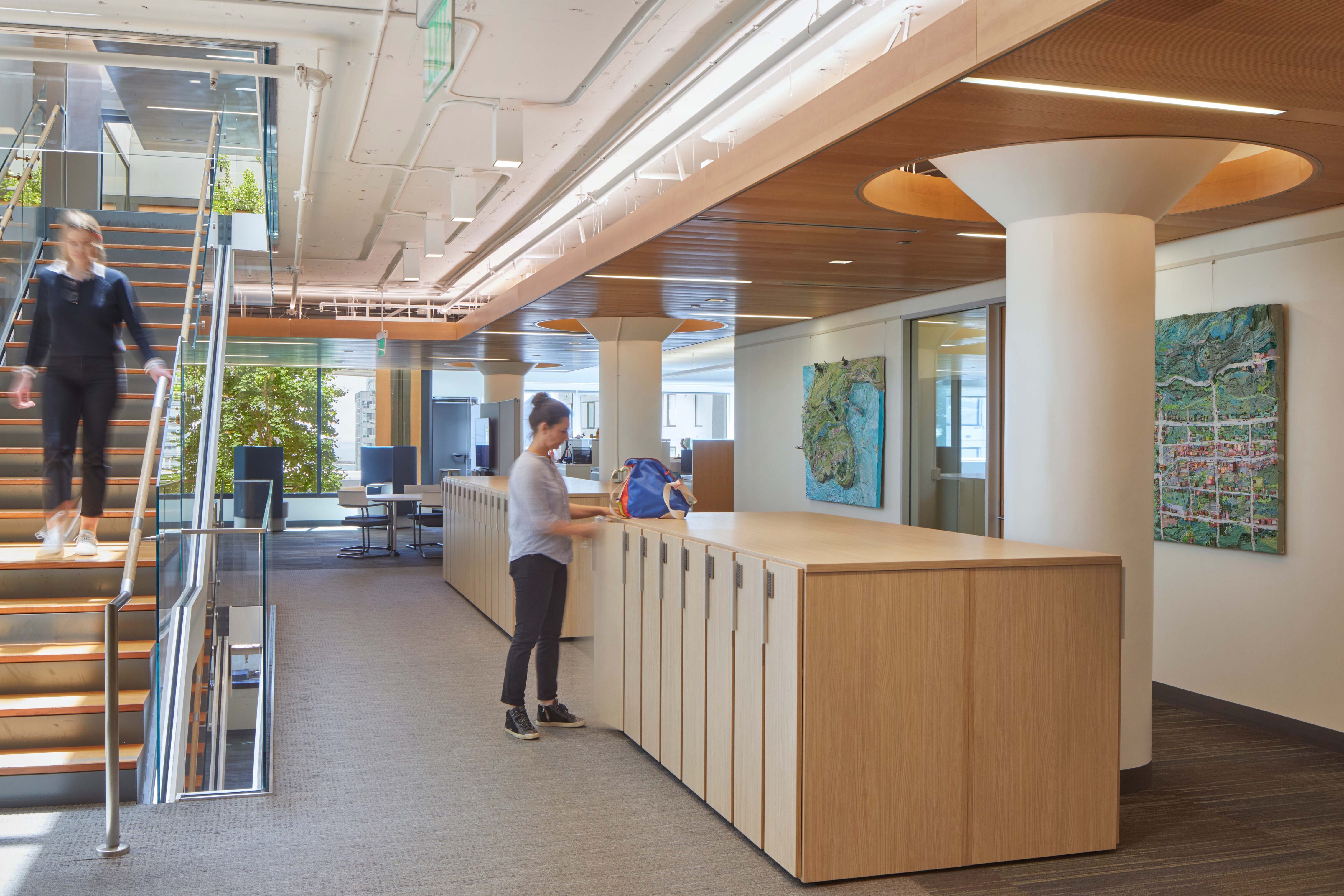 Interior office workspace with a central stair, wood ceiling accents, integrated storage, and large windows bringing daylight into an open, collaborative work area.