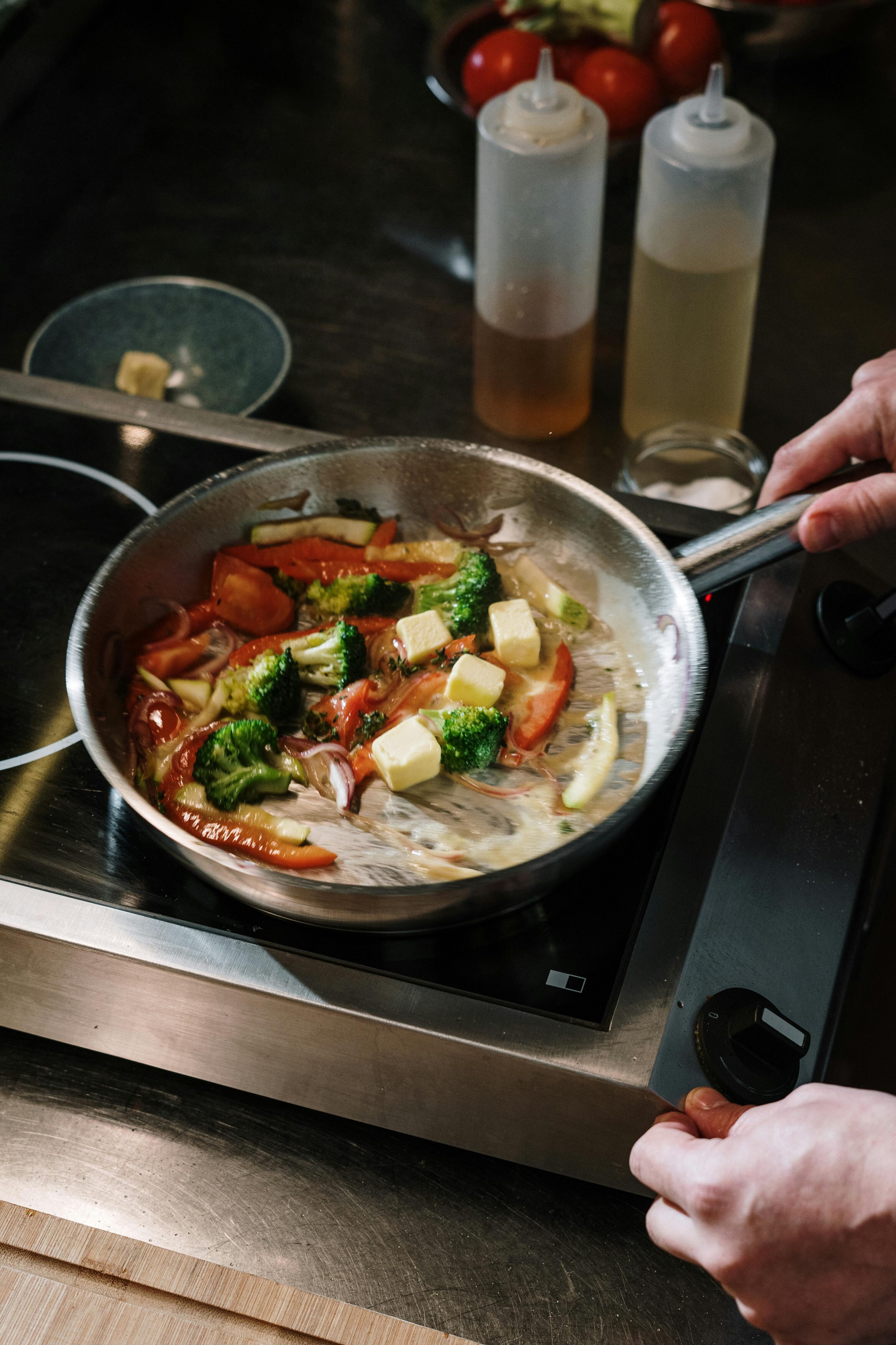 A person's hands cooking vegetables in a pan on a portable stove.