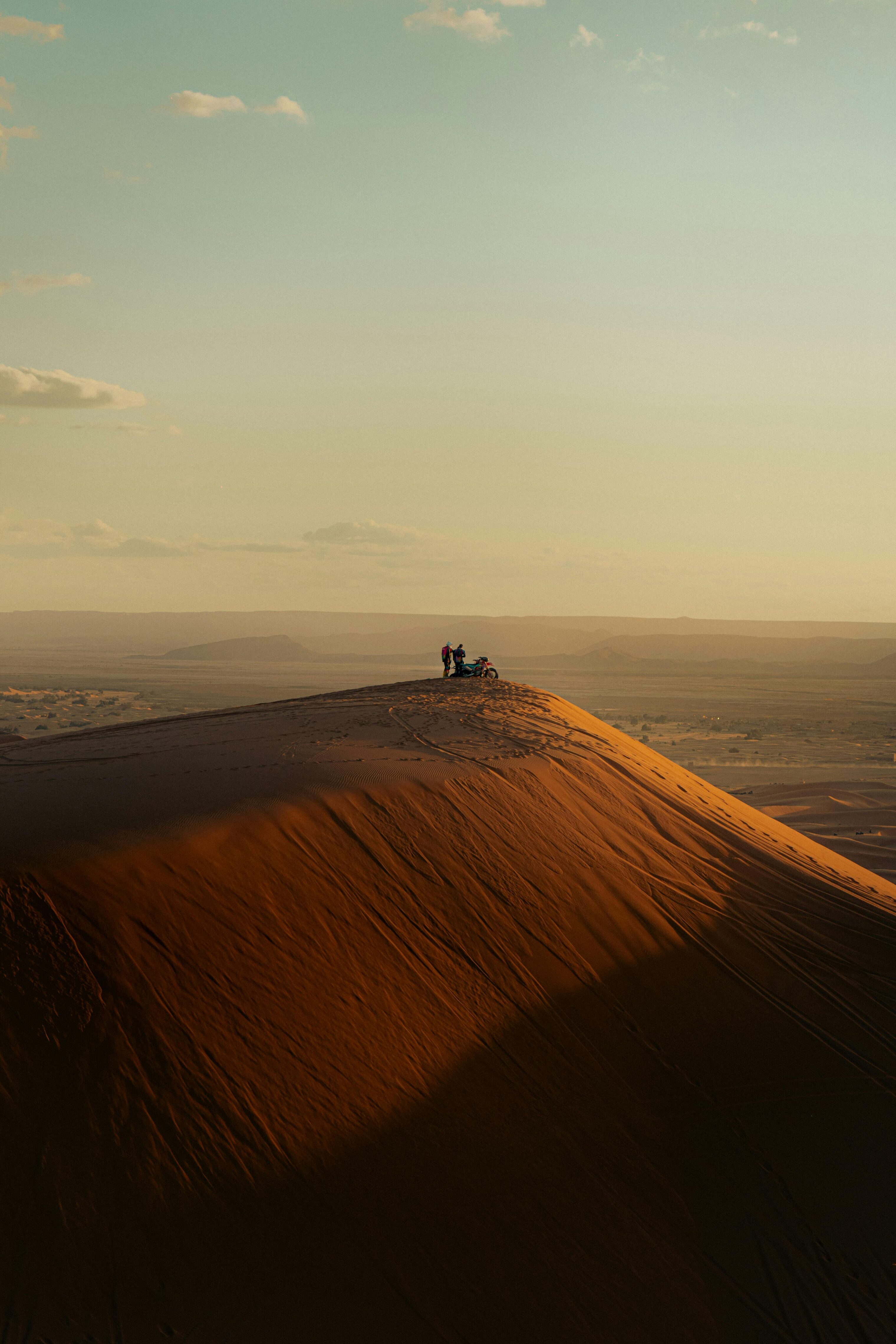 A sand dune from afar. People with an ATV stand on the top.