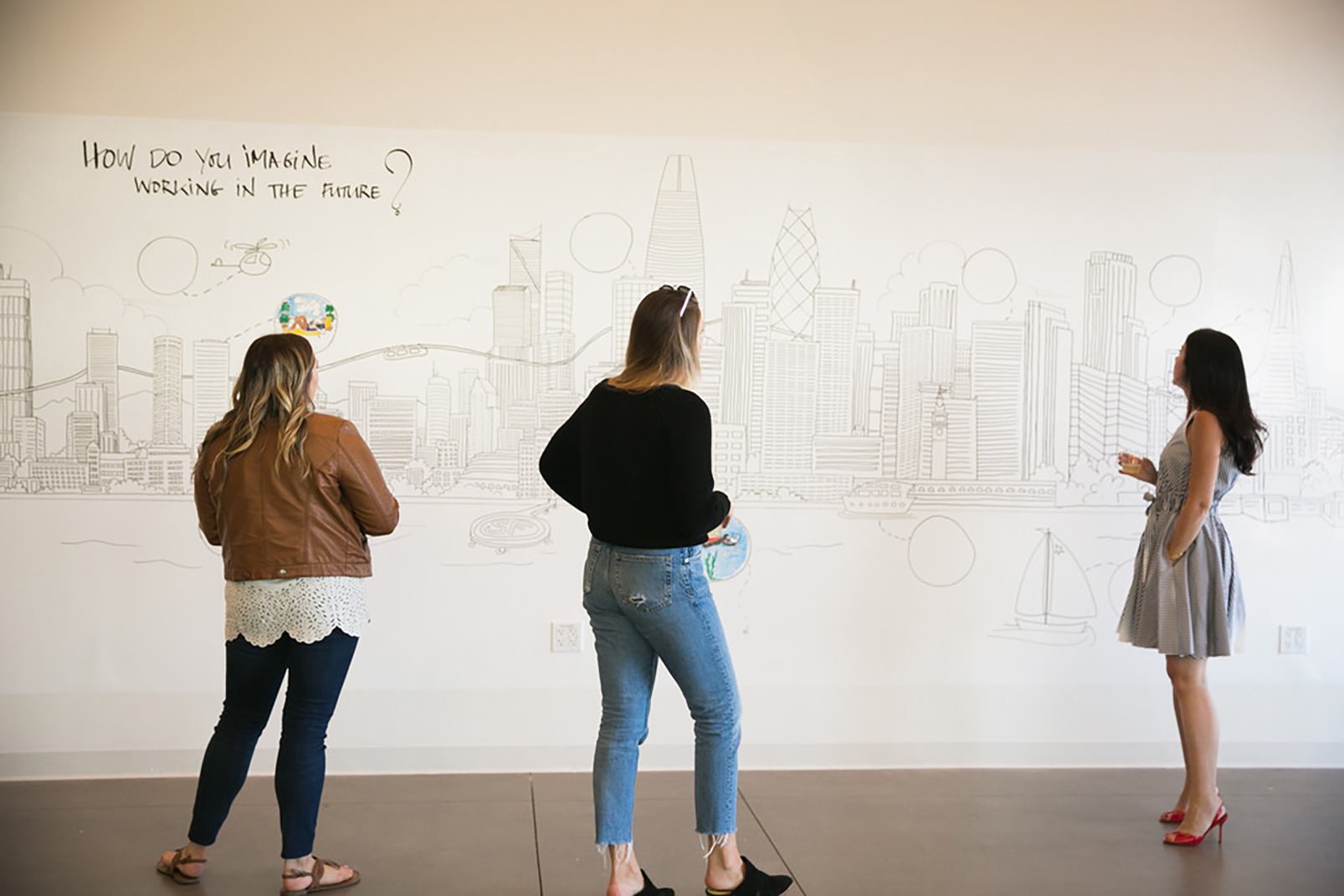 Three people adding ideas to a wall mural of the San Francisco skyline under the prompt “How do you imagine working in the future?”
