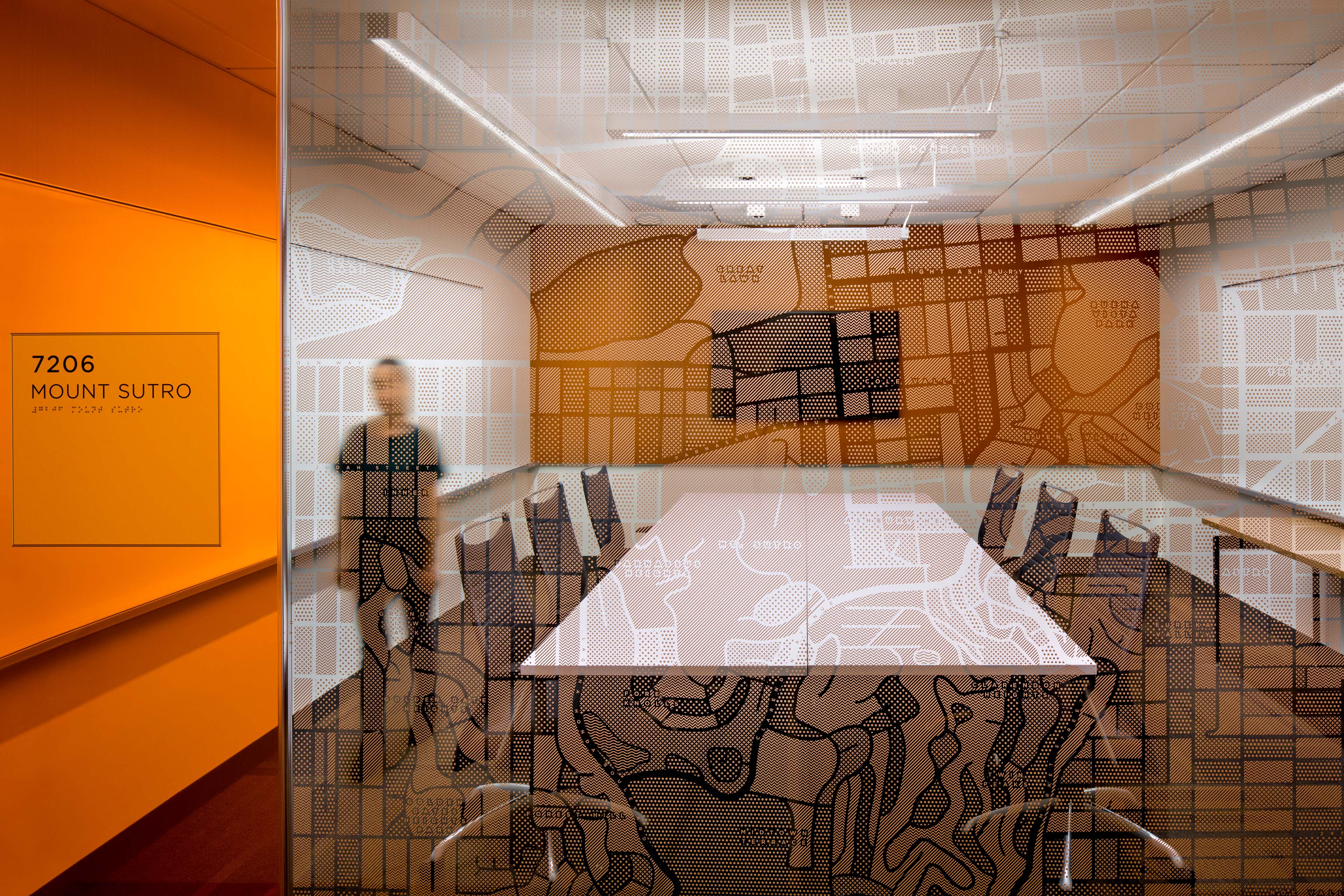 Glass-walled meeting room with a Mount Sutro map graphic, orange wall signage, and a conference table visible through patterned glazing.