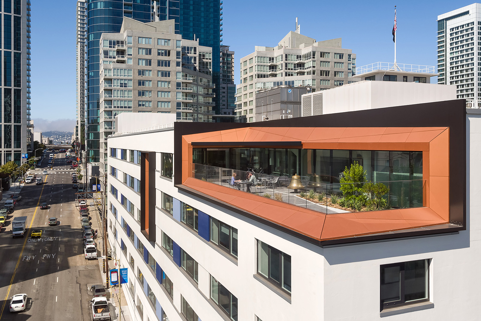 Rooftop office terrace with seating and planted areas, framed by orange metal cladding and surrounded by downtown San Francisco high-rises.