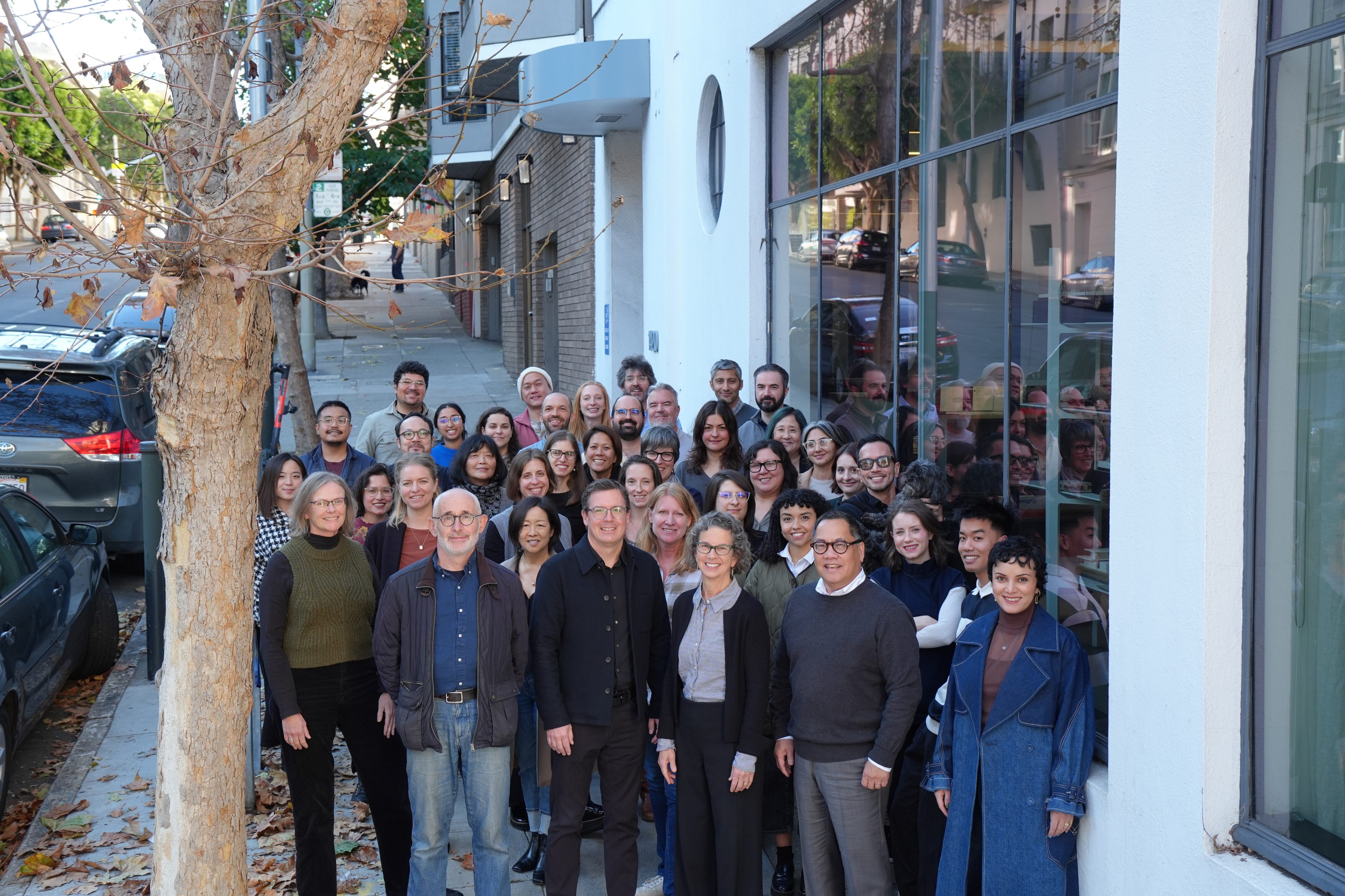 Group of TEF staff standing together on sidewalk outside office with a tree on the left.