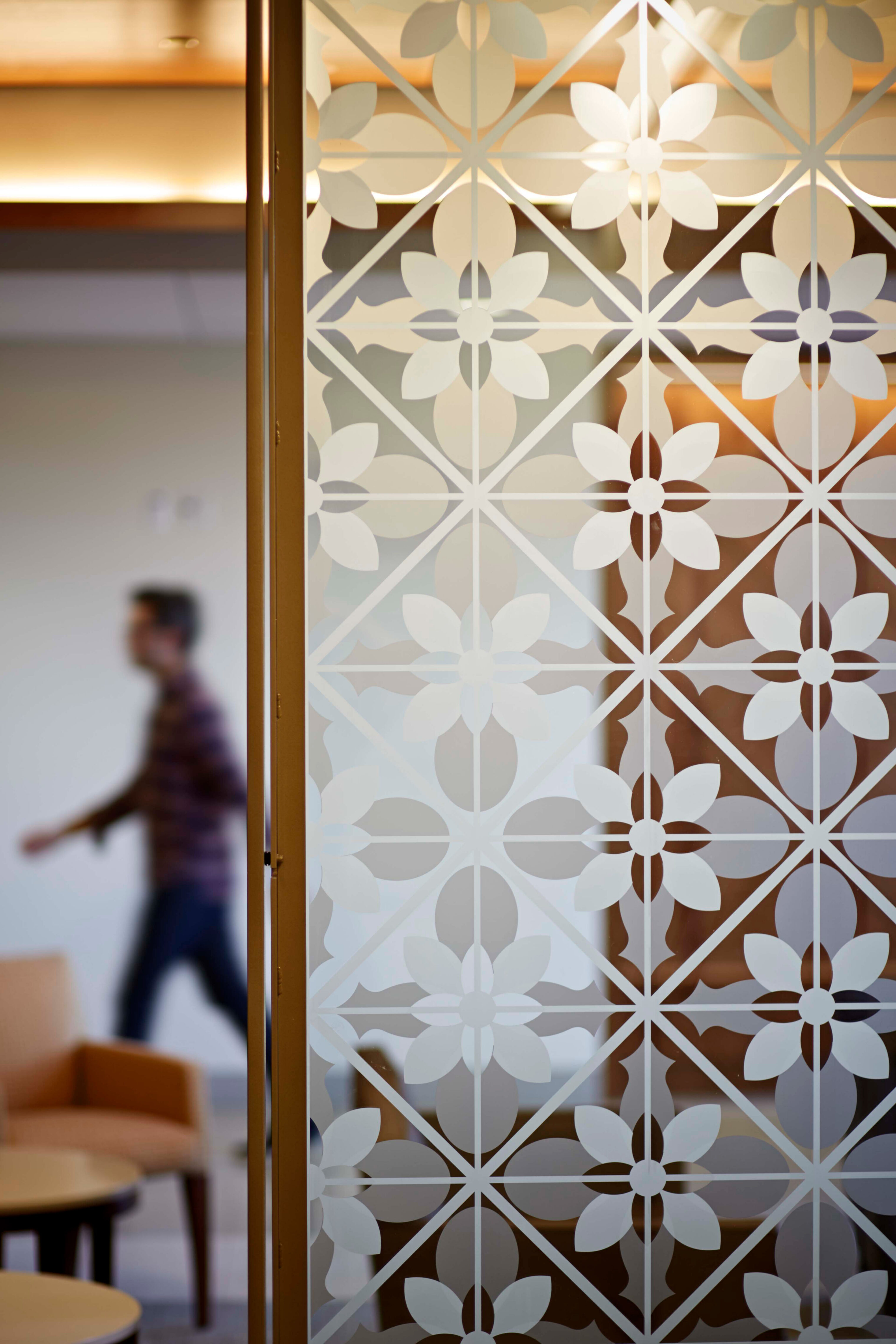 Decorative frosted glass screen with a geometric floral pattern, with a blurred person walking through the interior beyond.