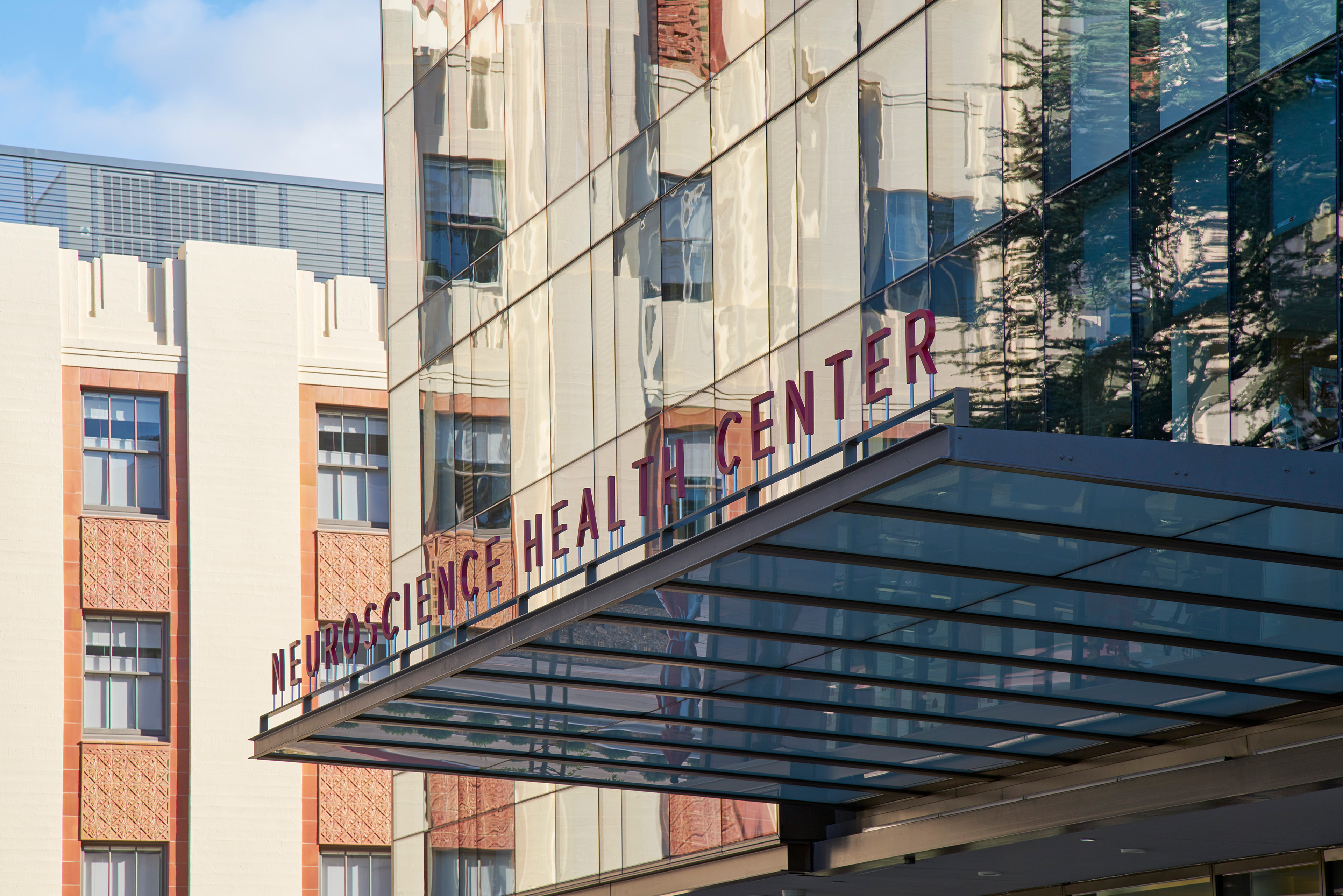 Close-up of the Neuroscience Health Center entrance canopy and signage reflected across the building’s glass façade.