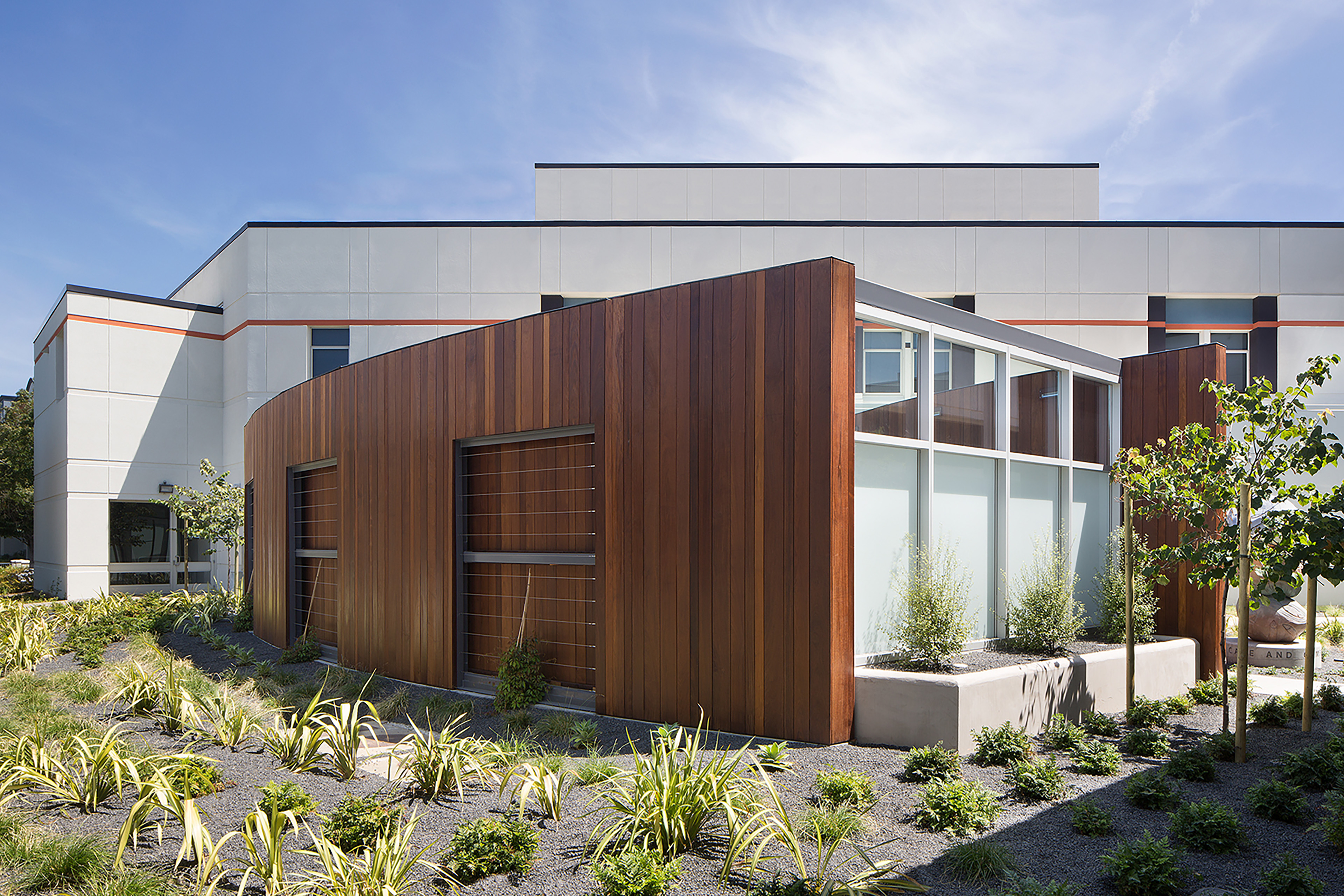 Modern hospital exterior with curved wood cladding, large windows, and drought-tolerant landscaping.