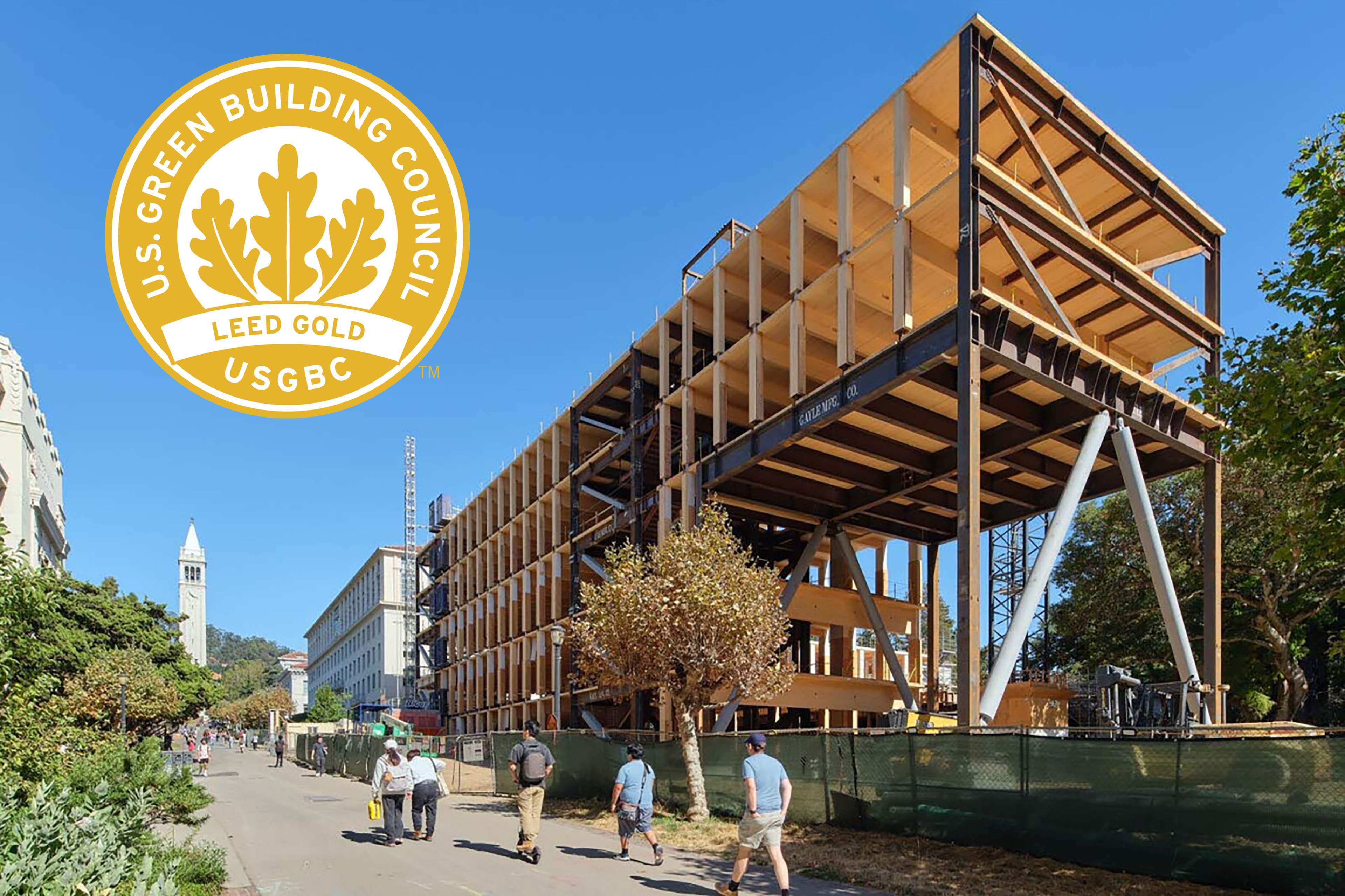 A steel-and-timber academic building under construction on a university campus, with a LEED Gold certification logo in the upper left.
