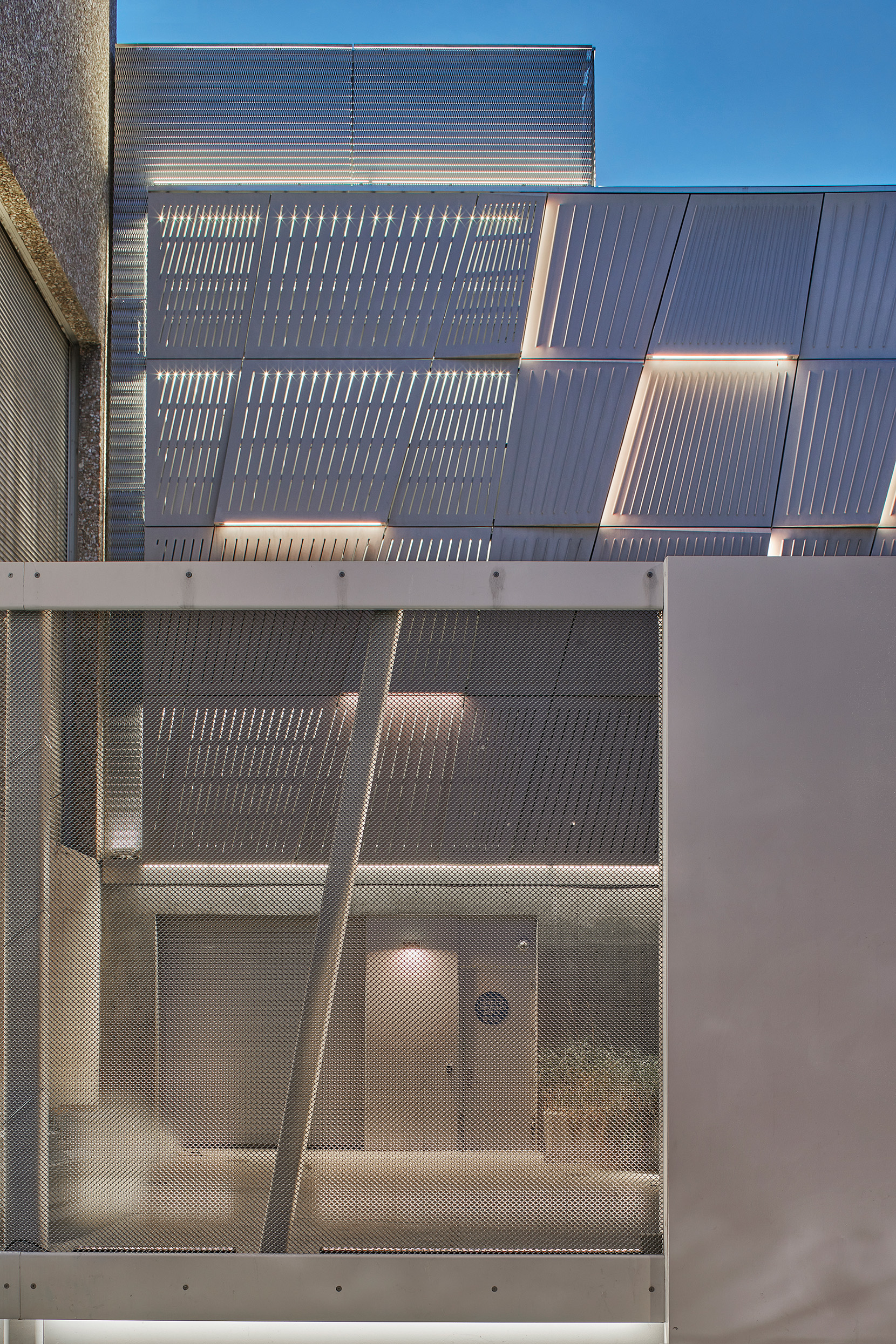 Architectural detail of perforated metal façade panels and a screened service enclosure, with linear lighting highlighting the patterned surface.