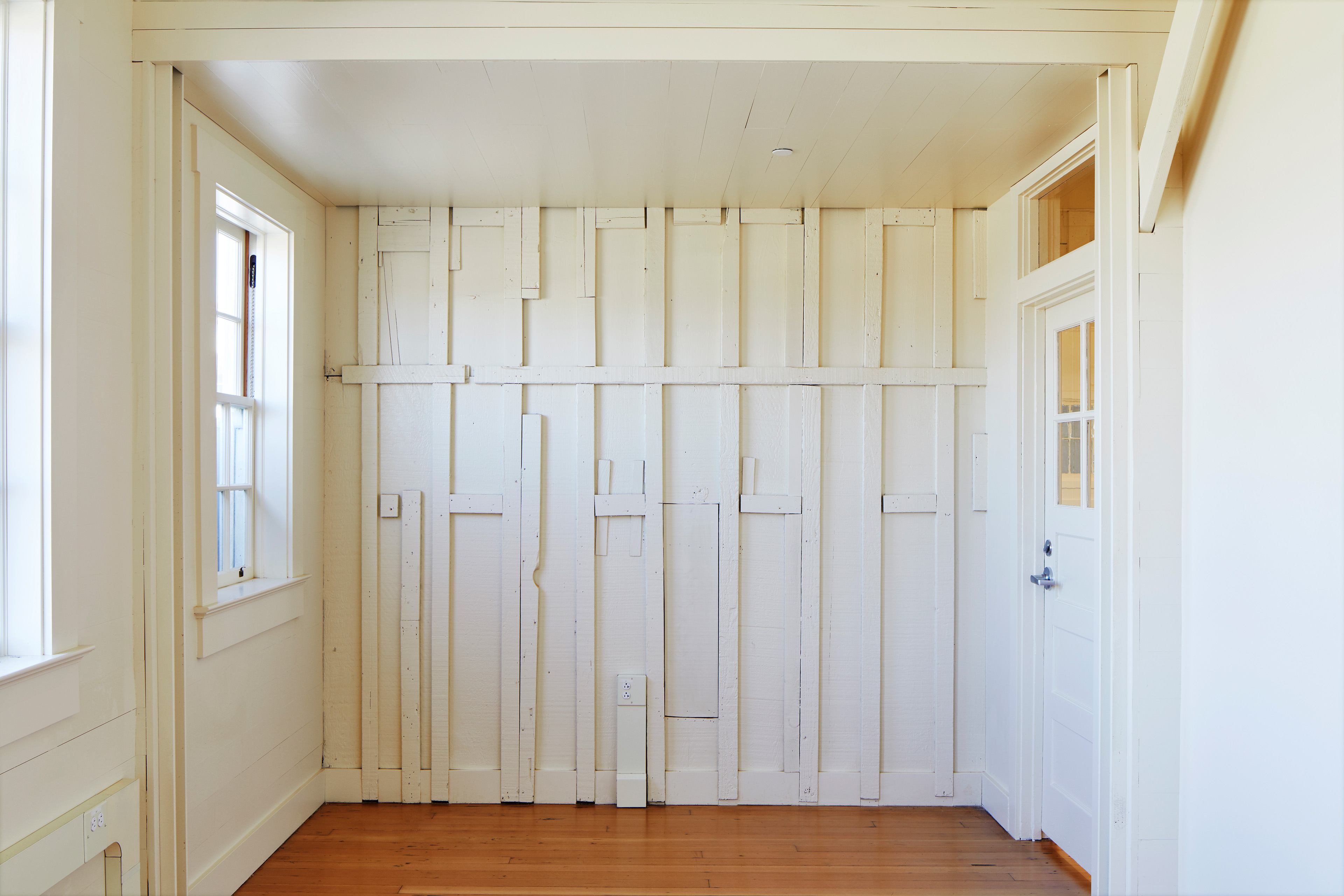 Bright restored interior with white-painted wood framing, hardwood floors, tall windows, and a glazed door.