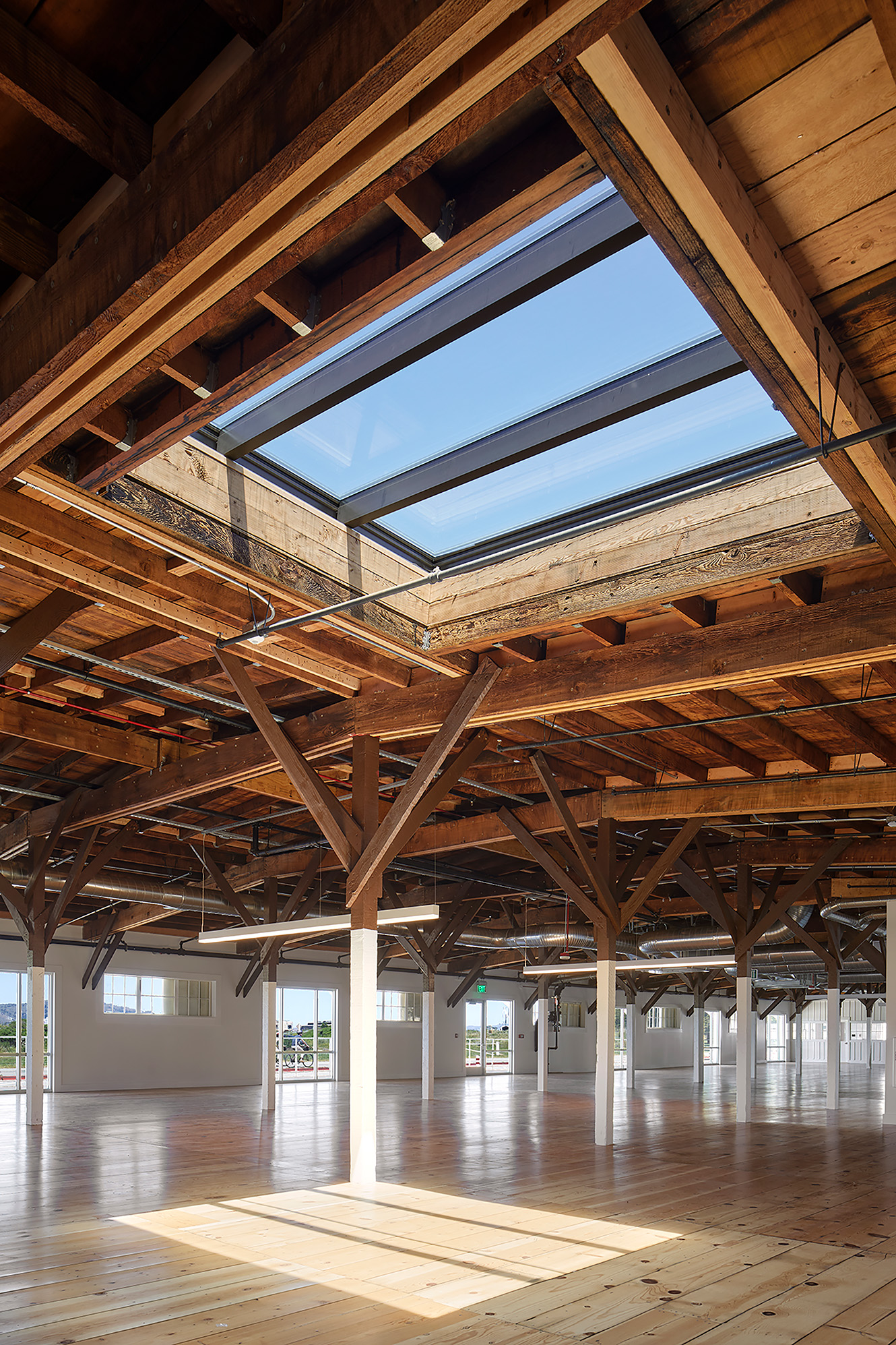 Open timber-framed interior with restored wood floors and a large skylight casting sunlight across the space.