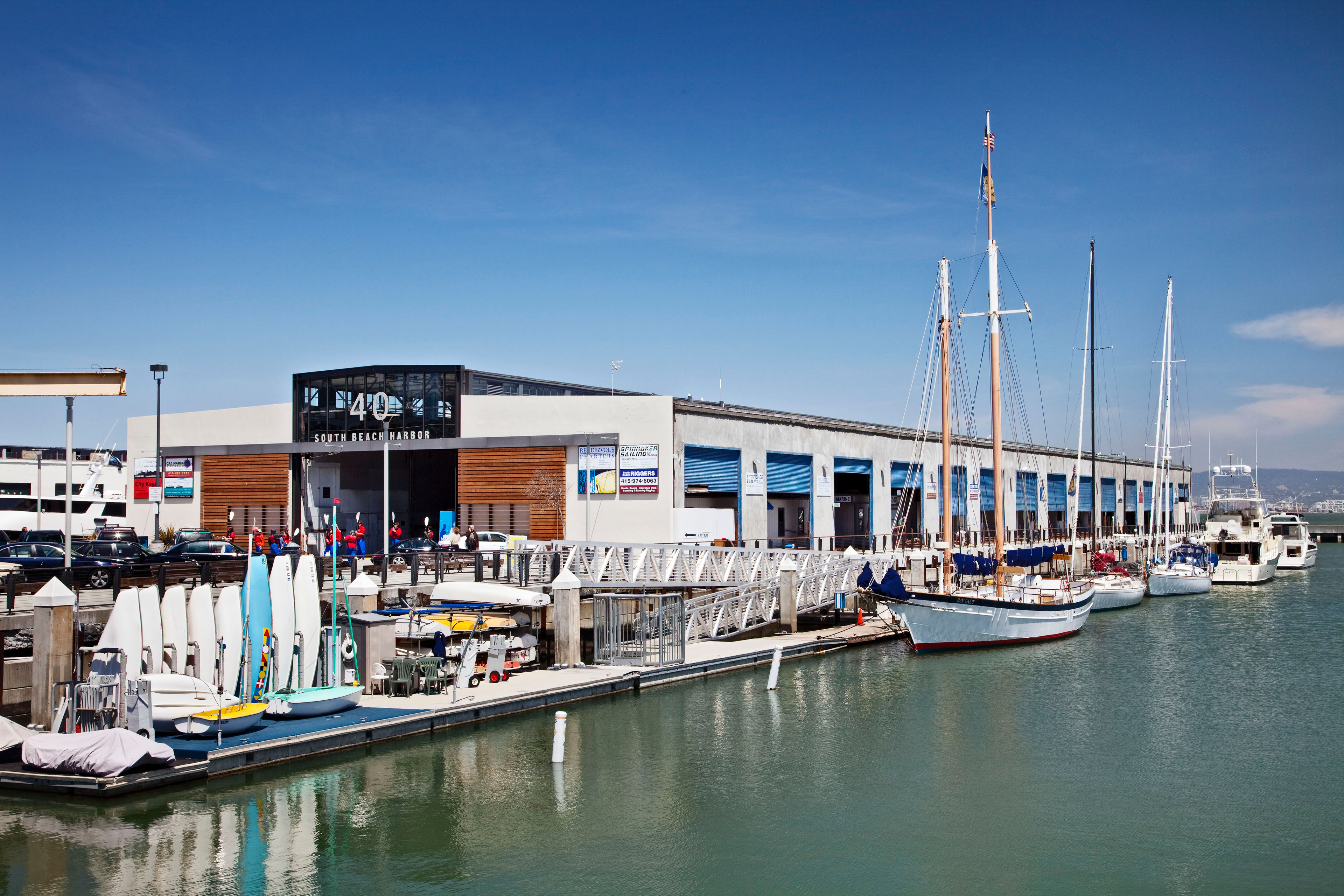 Sailboats dock beside a waterfront building at South Beach Harbor under a clear blue sky.