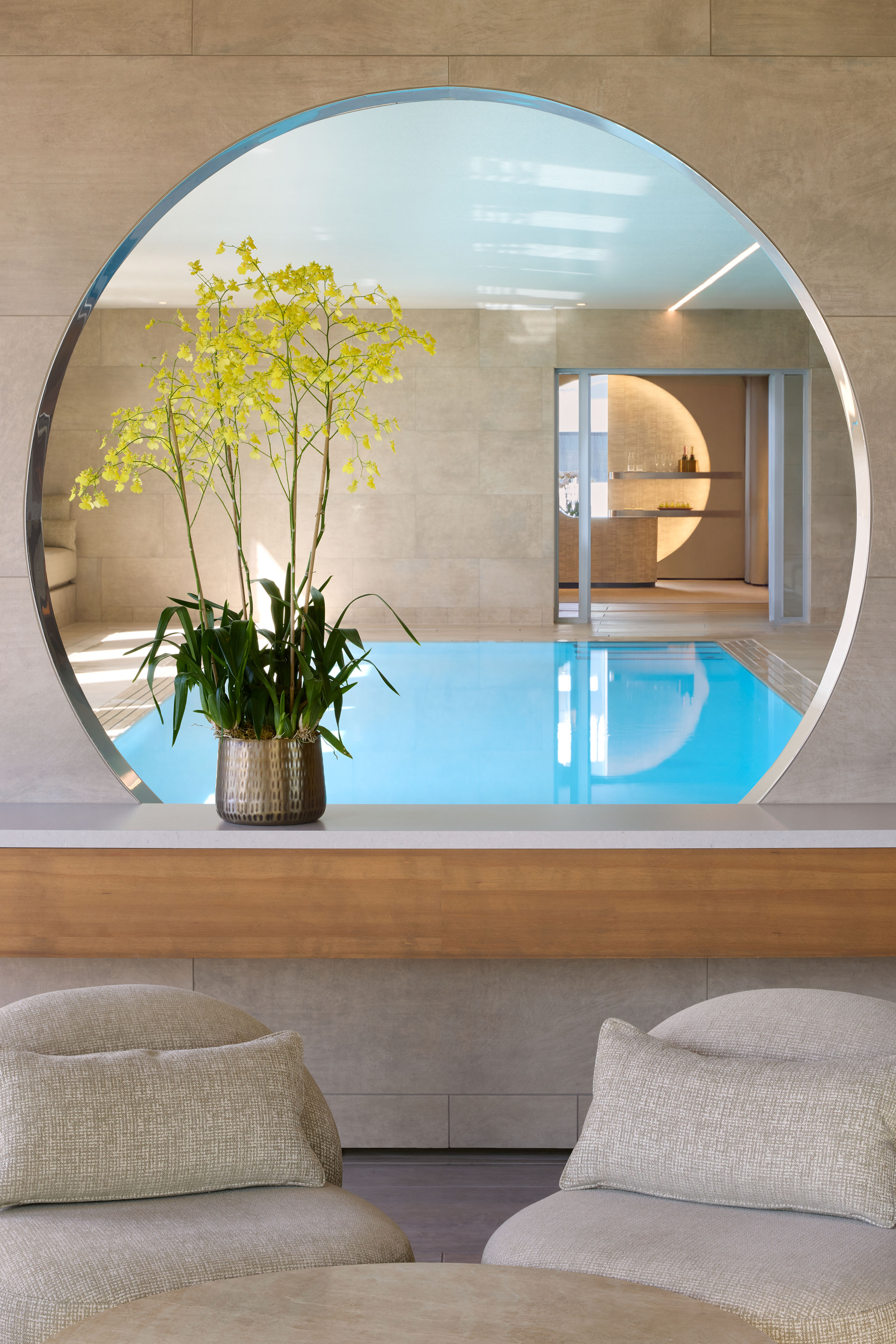 Circular opening frames an indoor pool and adjacent spa area, with yellow orchids and lounge seating in the foreground.