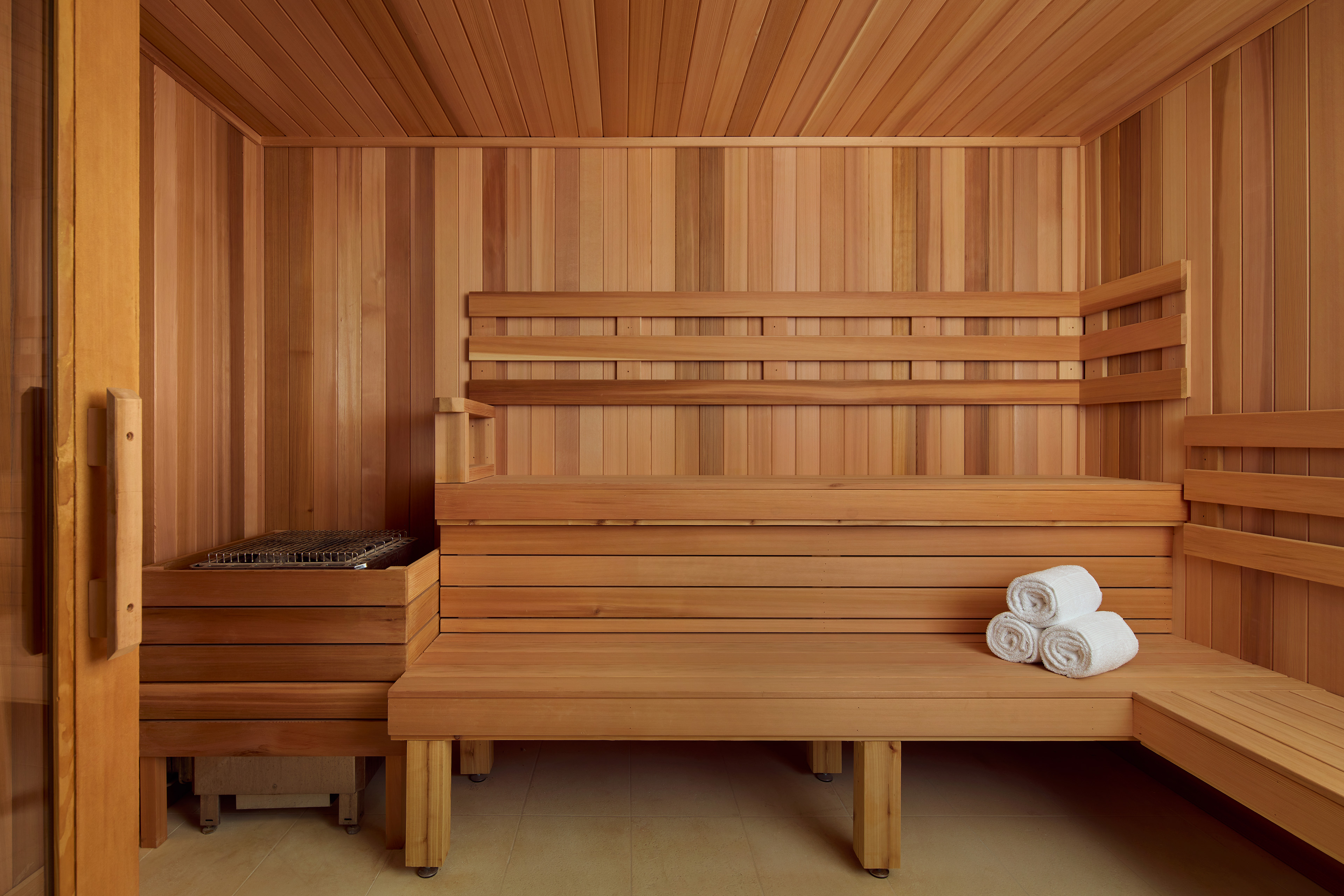 Wood-paneled sauna with tiered benches, a heater, and neatly rolled white towels.