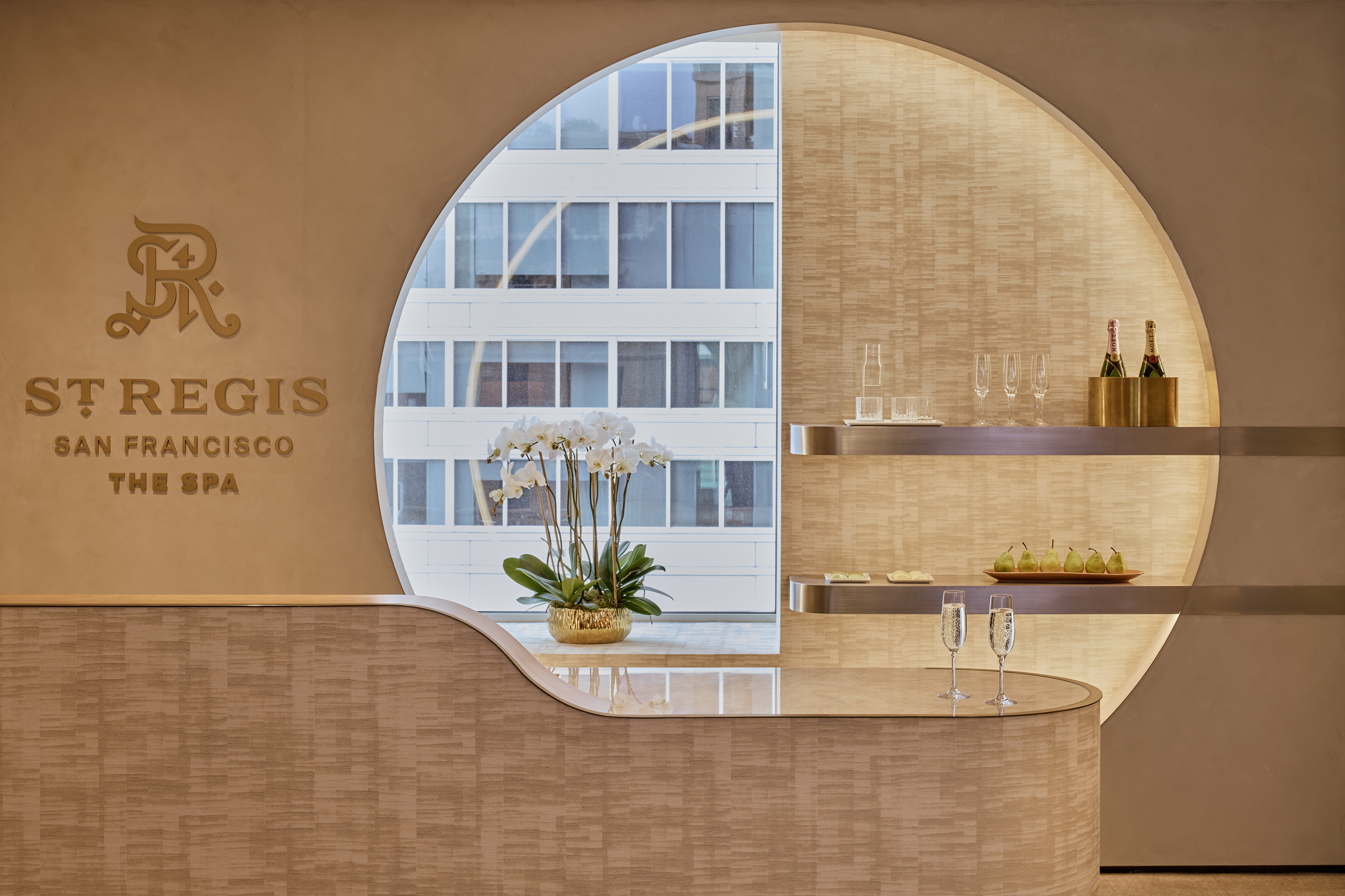 Reception desk at The Spa at The St. Regis San Francisco, with a large circular opening, orchids, integrated display shelves, and champagne service.