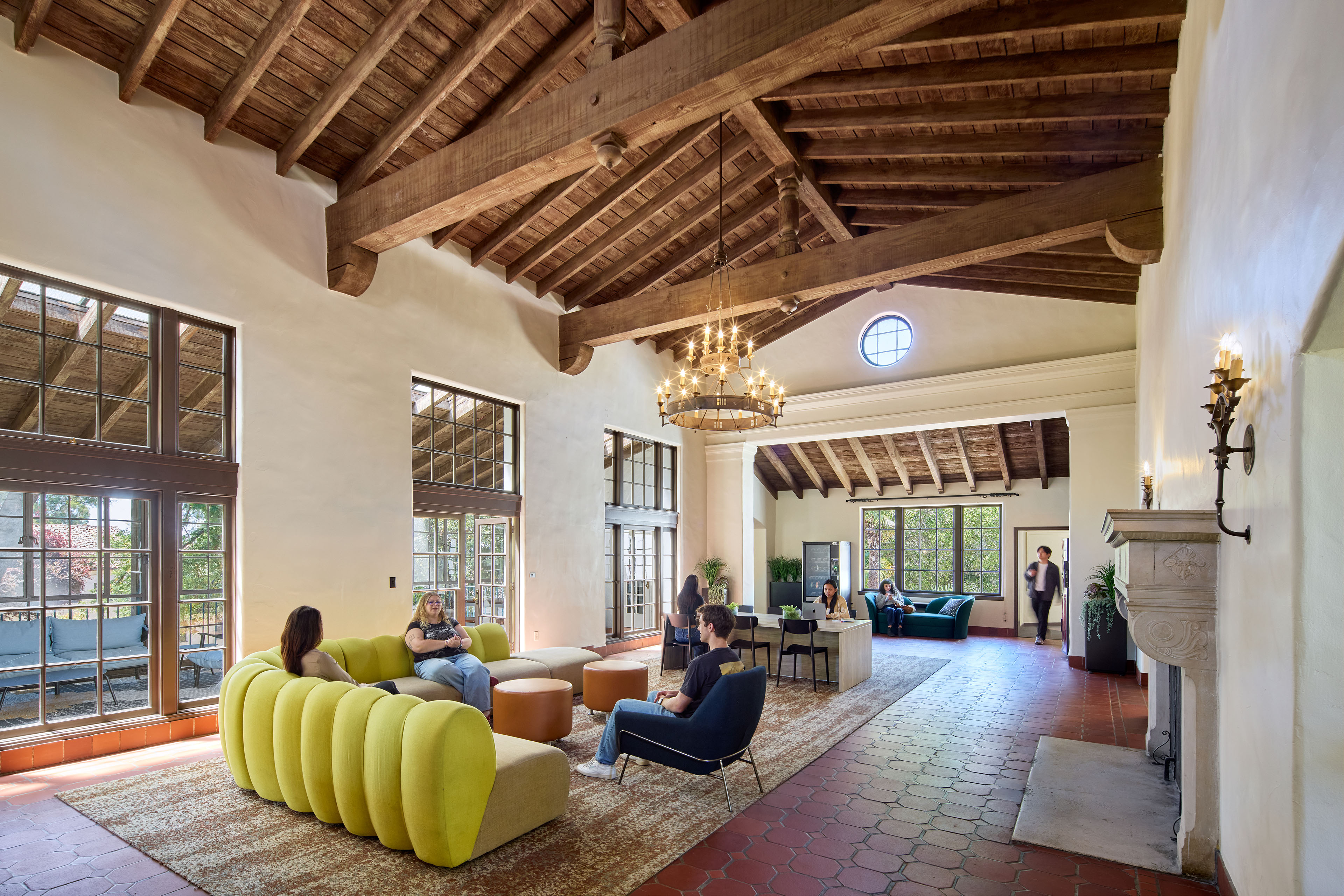 Historic student lounge with exposed wood beams, large windows, a fireplace, and contemporary seating, with students gathered throughout the space.